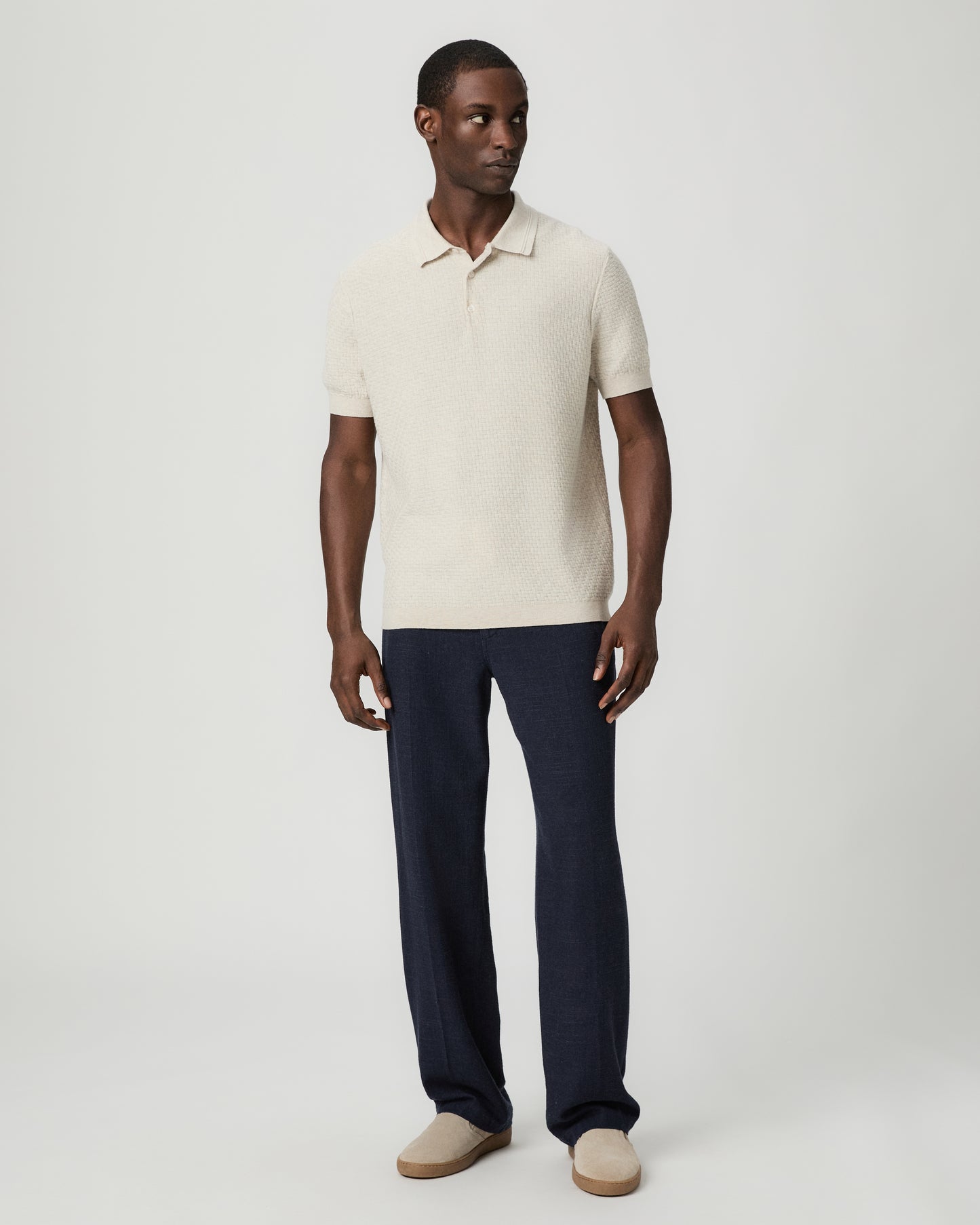 Man wearing a textured beige polo shirt with blue pants against a plain background