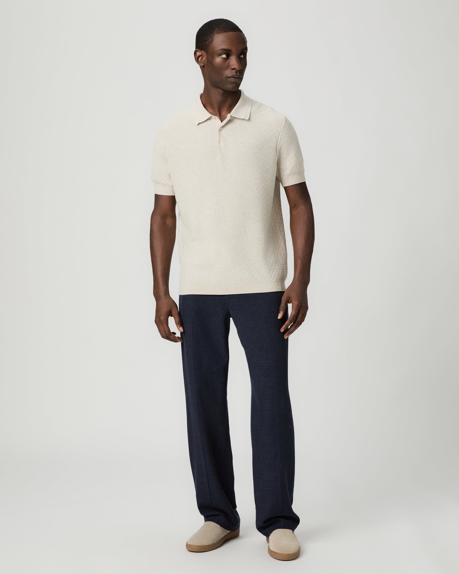 Man wearing a textured beige polo shirt with blue pants against a plain background