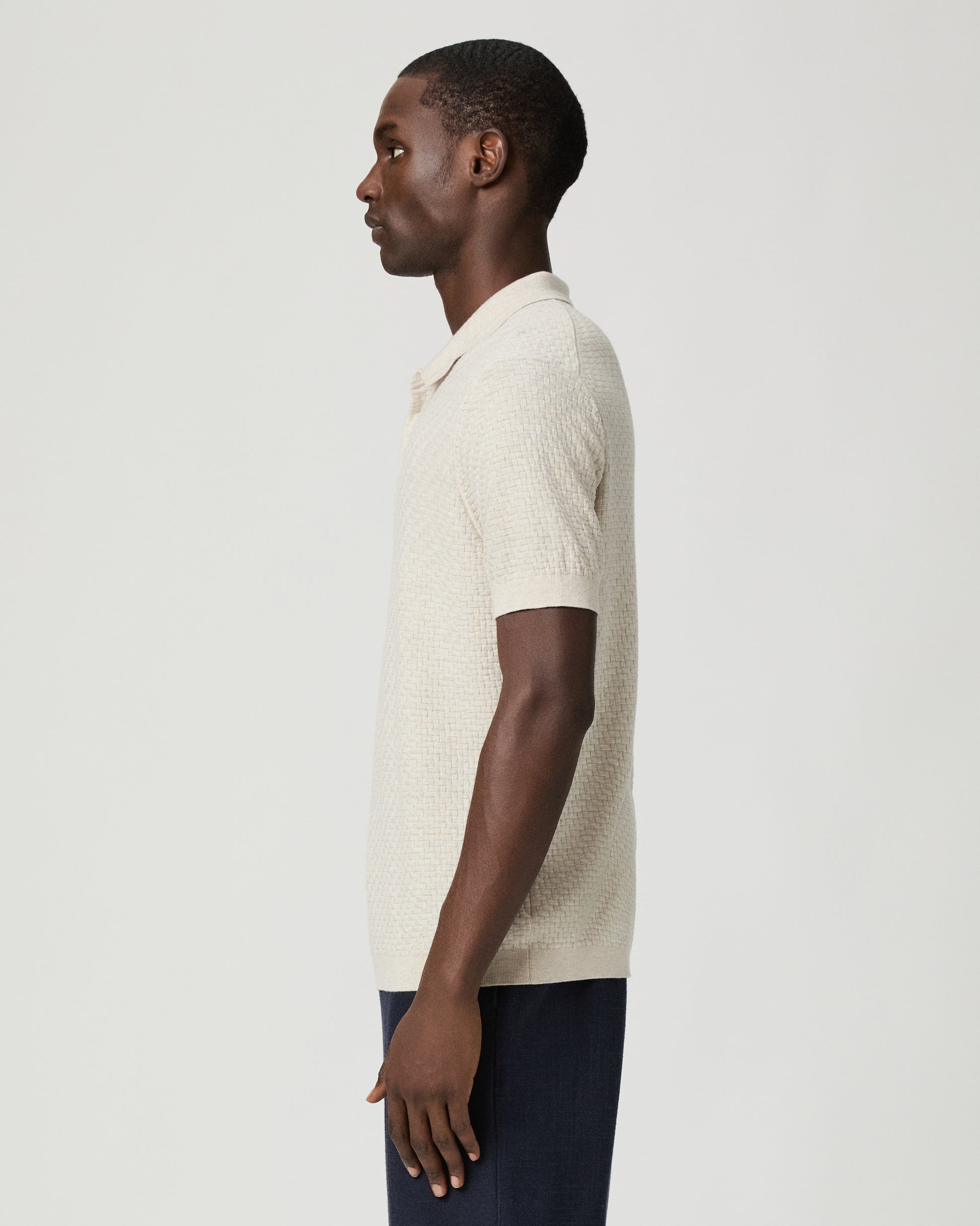 Man wearing a textured beige polo shirt with blue pants against a plain background