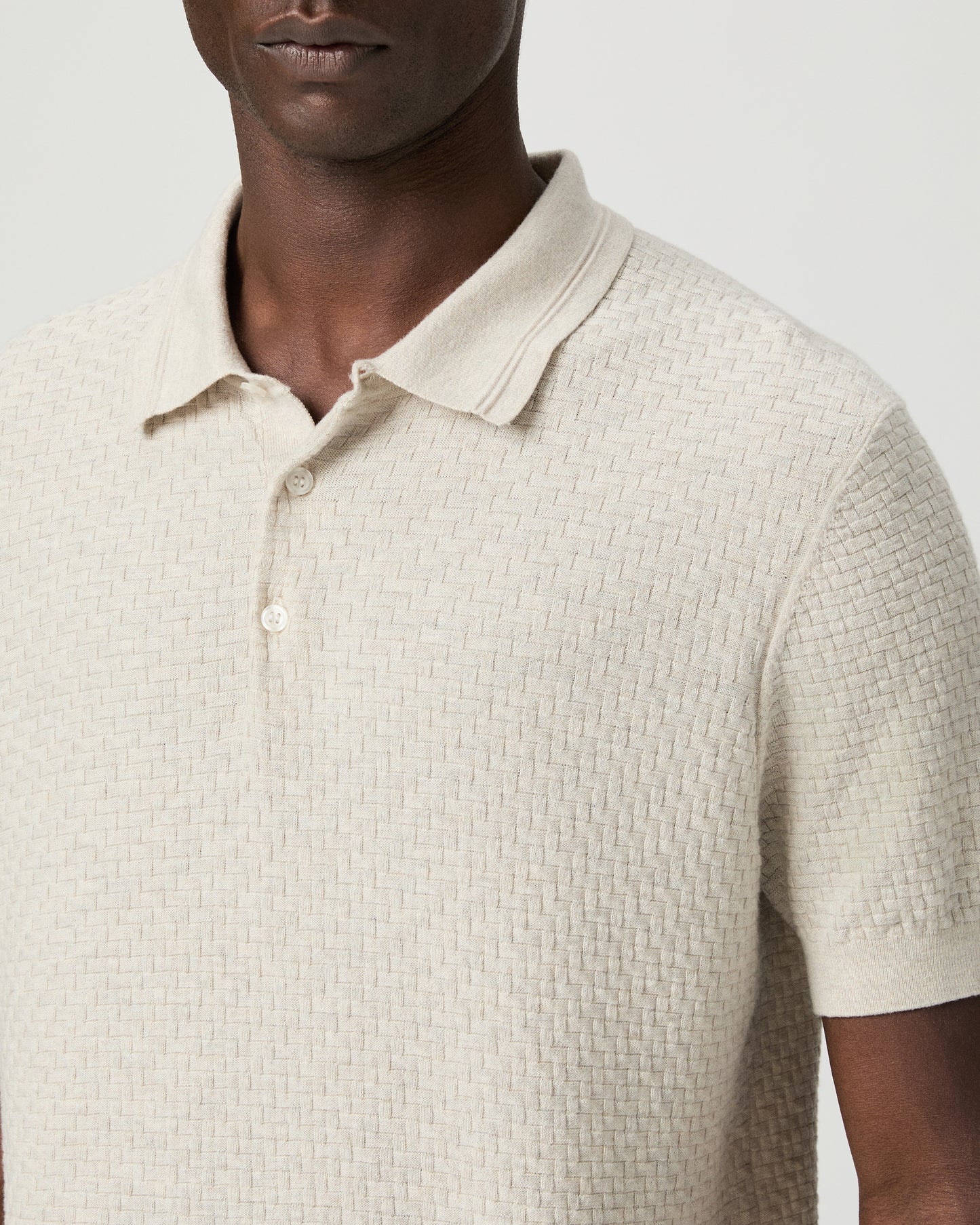 Man wearing a textured beige polo shirt with blue pants against a plain background