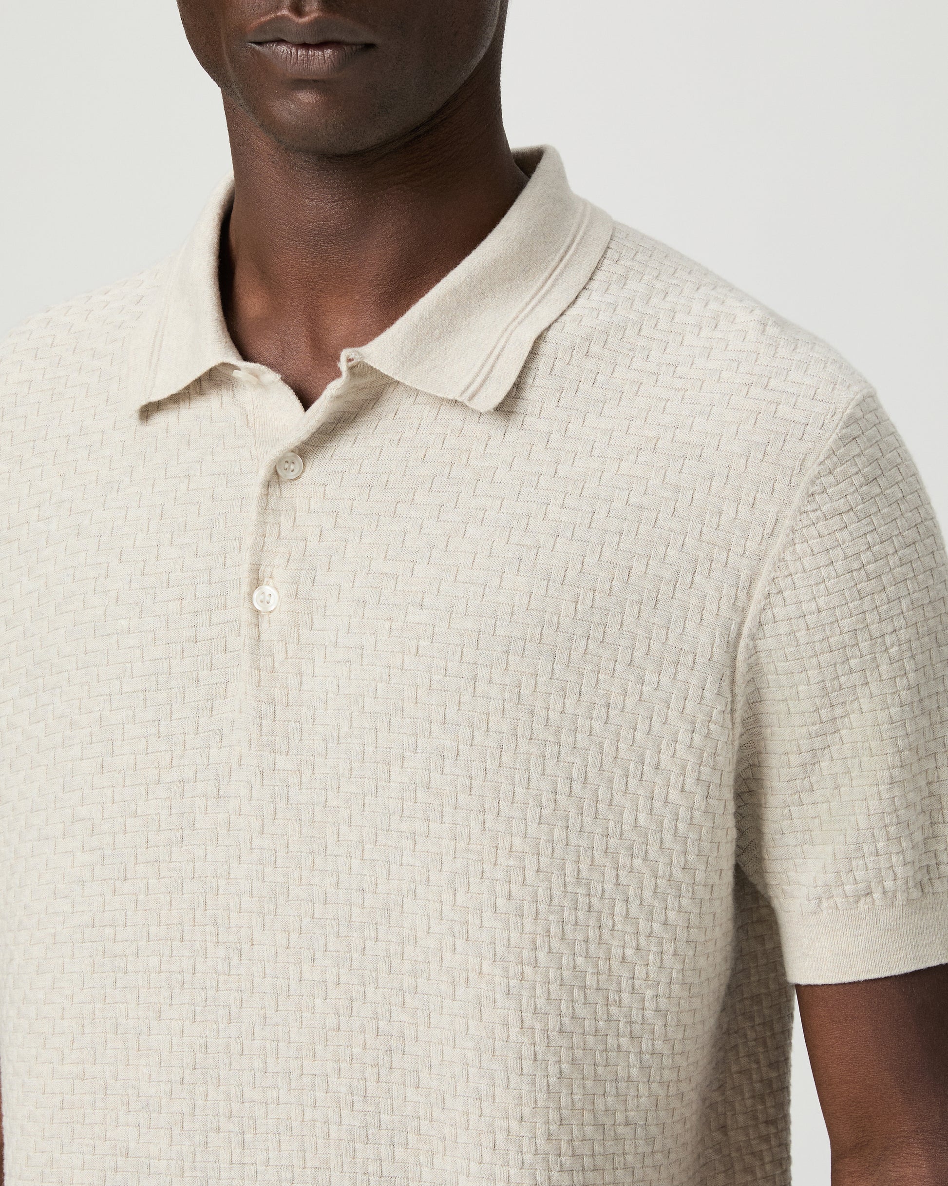 Man wearing a textured beige polo shirt with blue pants against a plain background