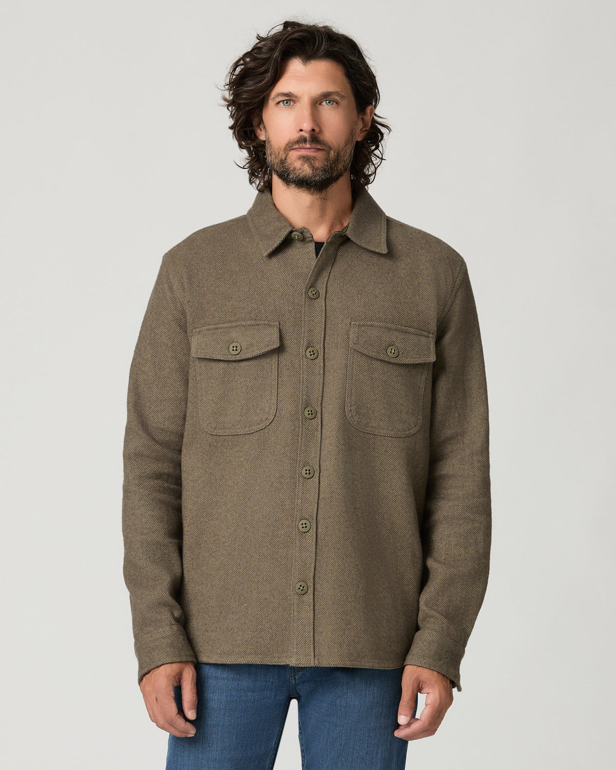 Portrait-style front view of a man with curly hair wearing the moss green textured Seymore overshirt buttoned closed, showing the flap chest pockets and collar.