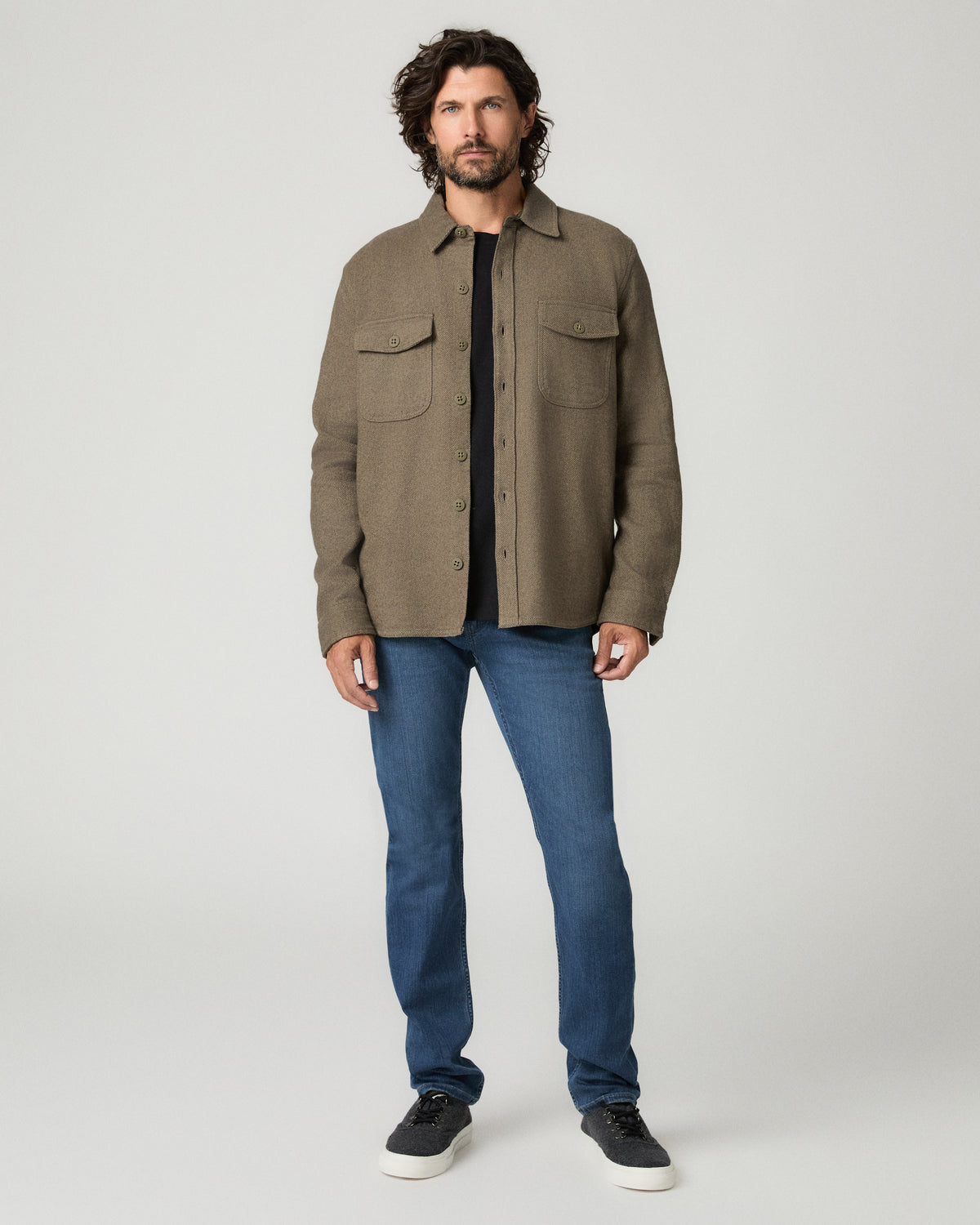 Full-length front view of the man wearing the moss green Seymore overshirt open over a white t-shirt, paired with dark wash straight jeans and white sneakers.