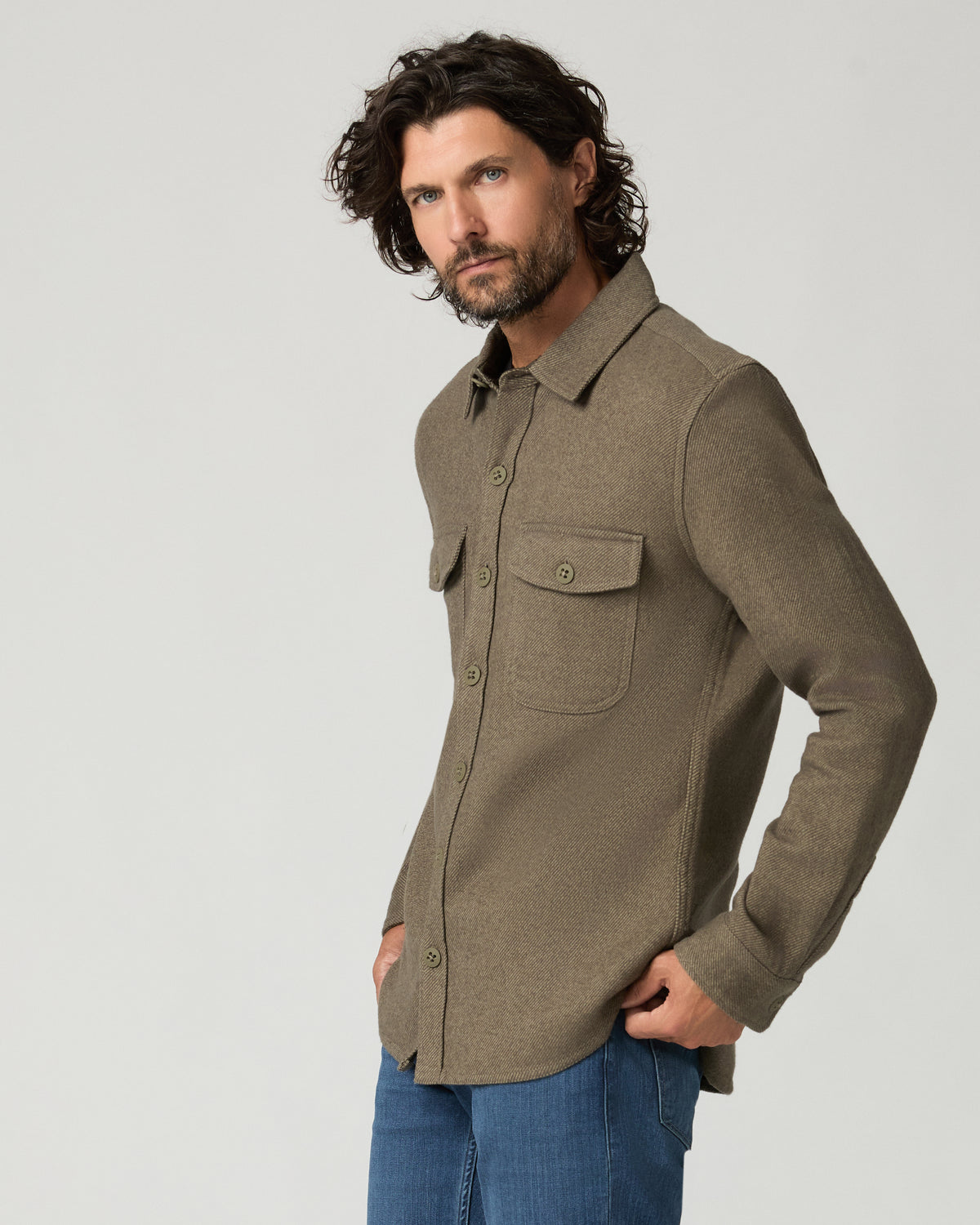Close front view of the moss green overshirt's chest pocket and button placket, hand resting near the pocket.