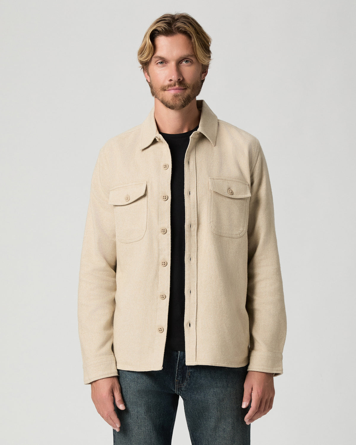 Model standing with arms at his sides, wearing the Seymore Overshirt in Windrush Combo, a stone-colored overshirt with two chest flap pockets, open over a black tee with dark jeans