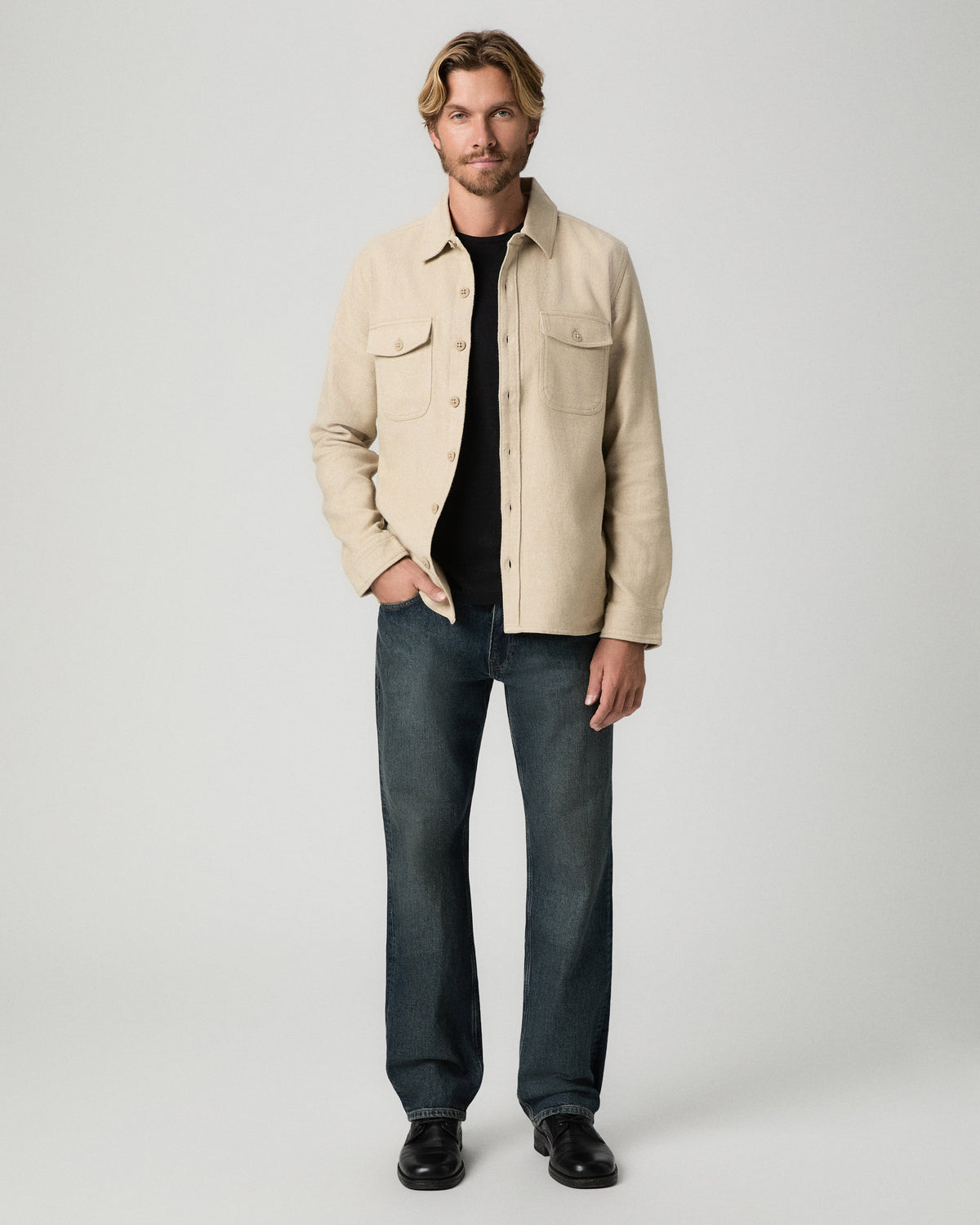 Full-length view of model with one hand in his pocket, wearing the Seymore Overshirt in Windrush Combo over a black tee with dark vintage-wash jeans and black boots