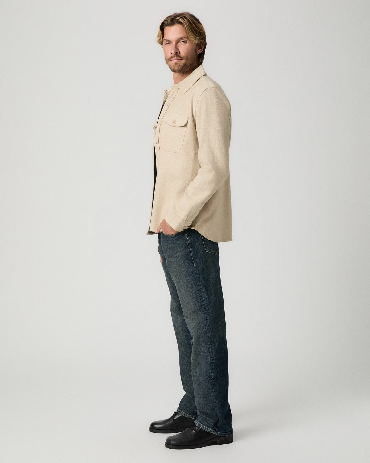 Side profile of model with one hand in his pocket, wearing the Seymore Overshirt in Windrush Combo with dark vintage-wash jeans and black boots