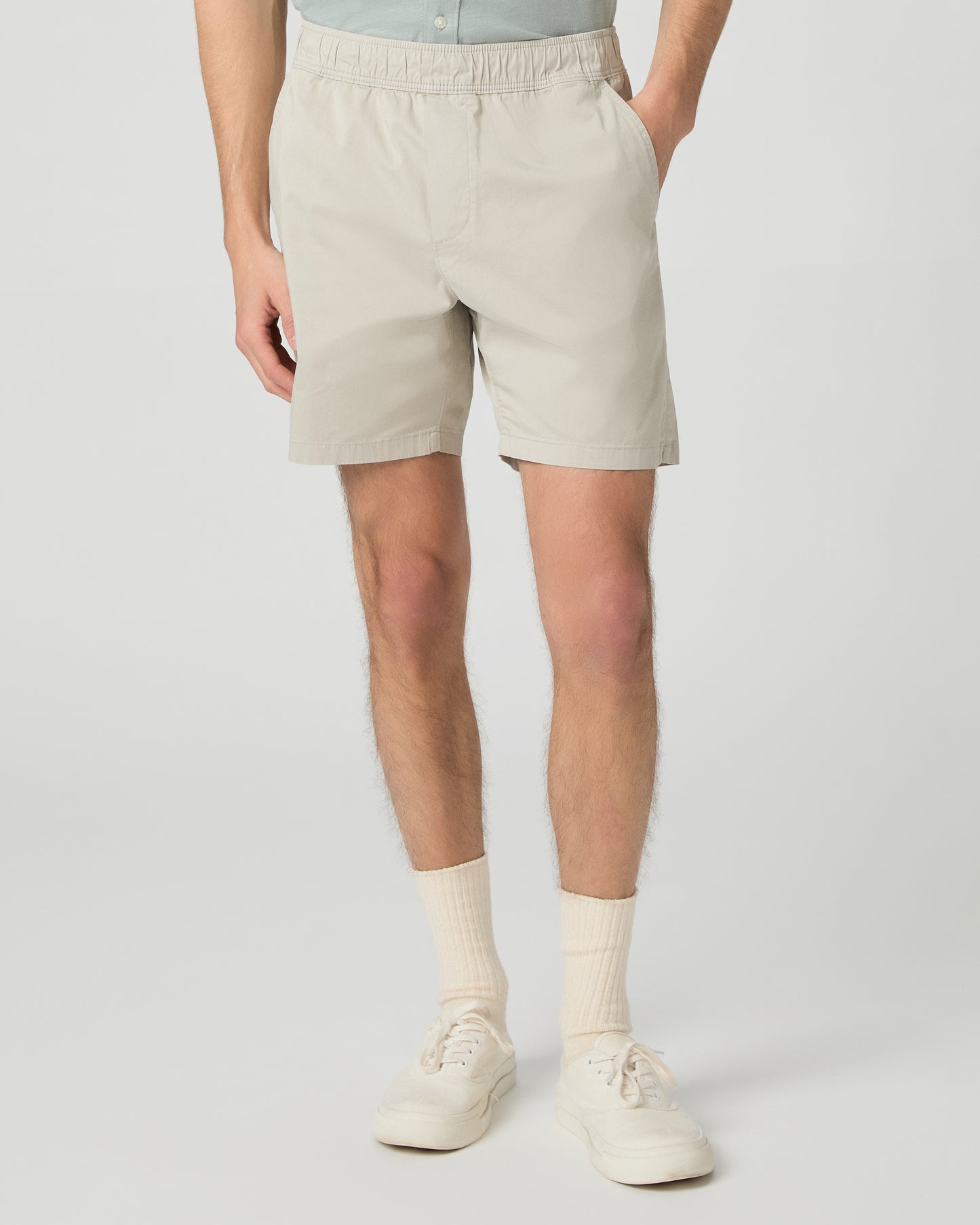 Man wearing a light green button-up shirt and beige shorts on a white background
