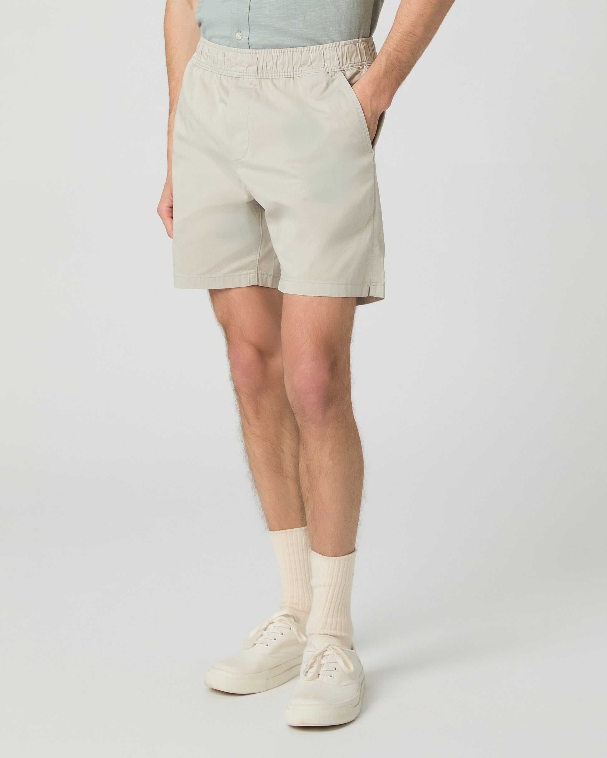 Man wearing a light green button-up shirt and beige shorts on a white background