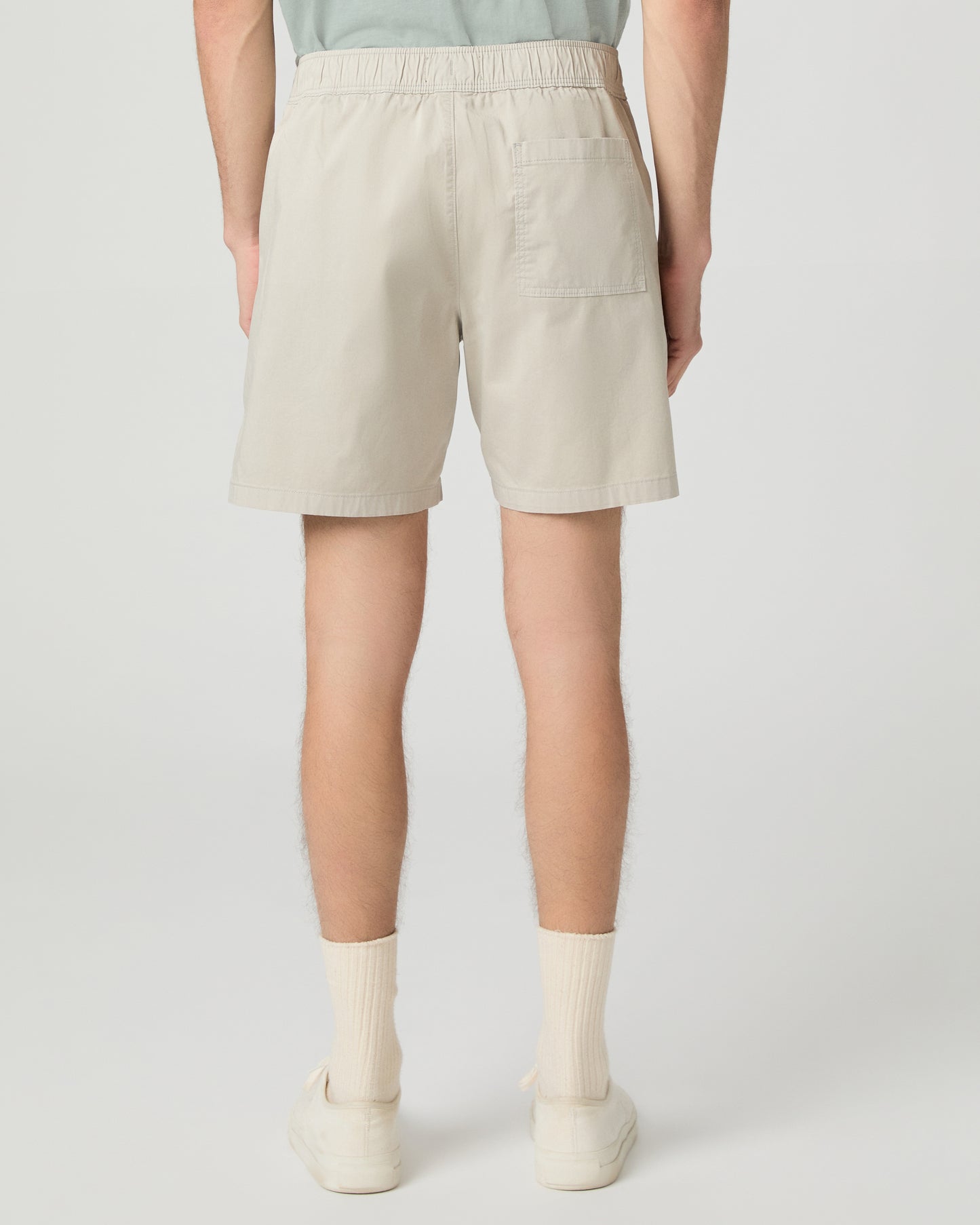 Man wearing a light green button-up shirt and beige shorts on a white background