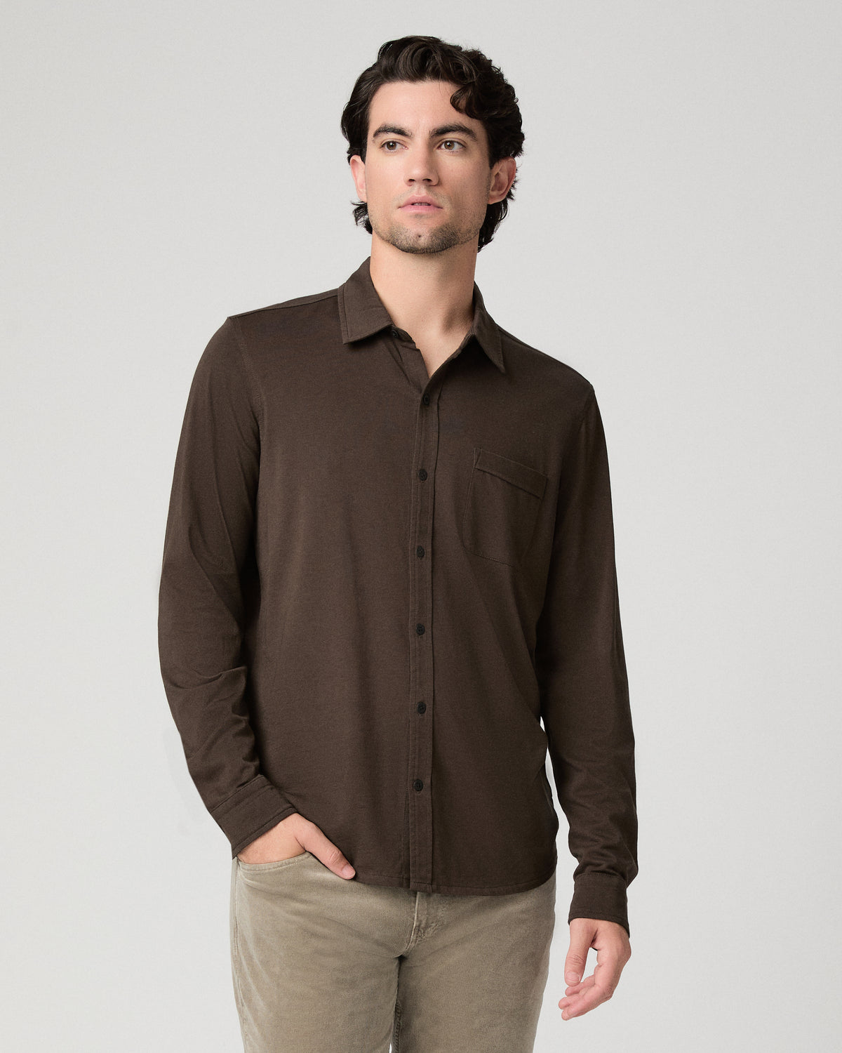 Man wearing a brown top and beige pants against a white background