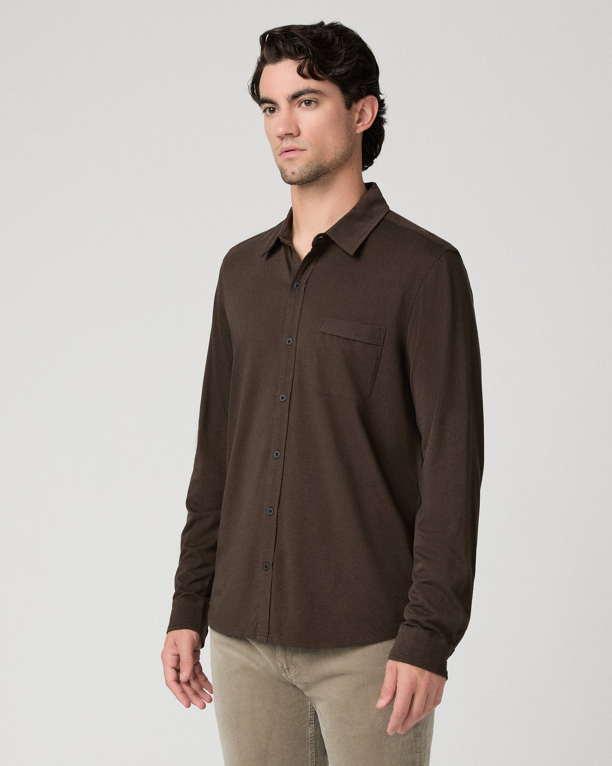 Man wearing a brown top and beige pants against a white background