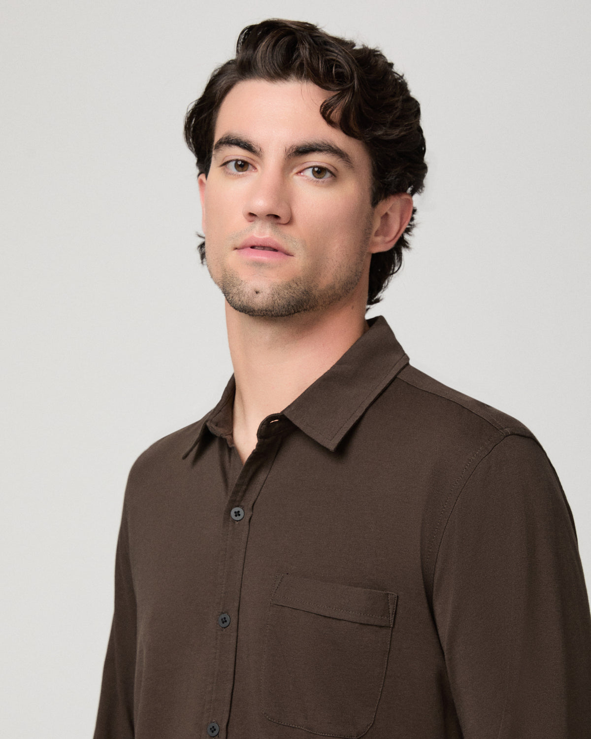 Man wearing a brown top and beige pants against a white background