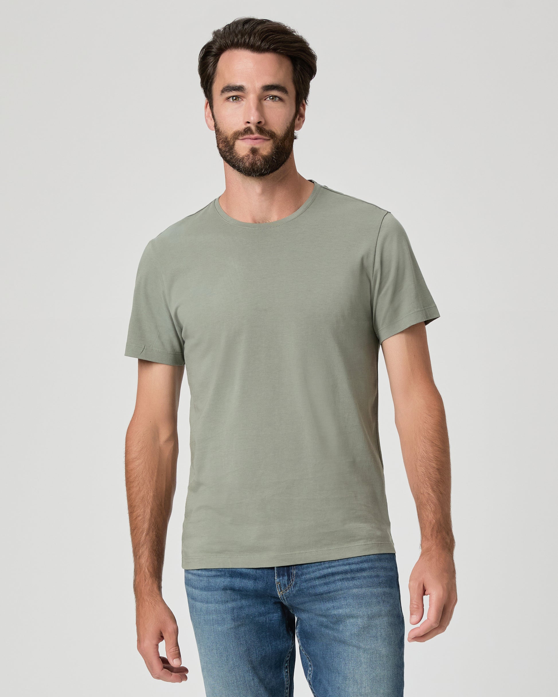 Man wearing a plain green t-shirt and blue jeans on a light gray background