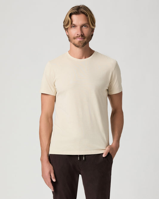 Model standing with one hand in his pocket, wearing the Sorden Crew Neck Tee in Light Pale Antler, a cream short-sleeve tee, with dark brown pants