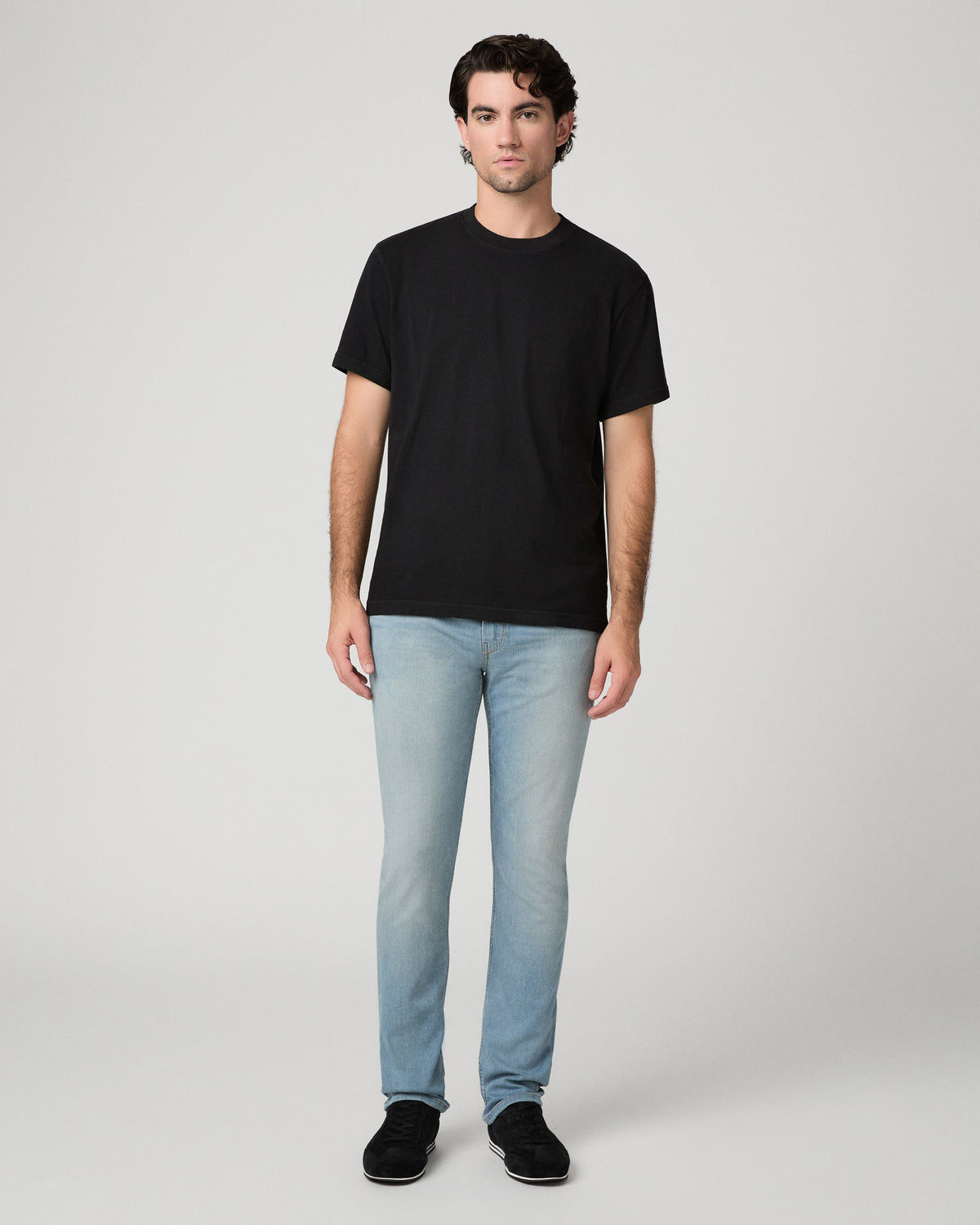 Man wearing black tee and light wash jeans against a black background