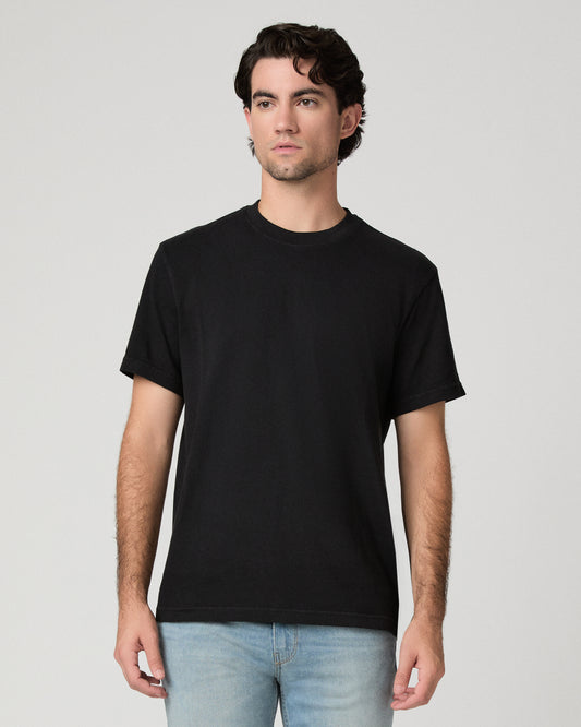 Man wearing black tee and light wash jeans against a black background