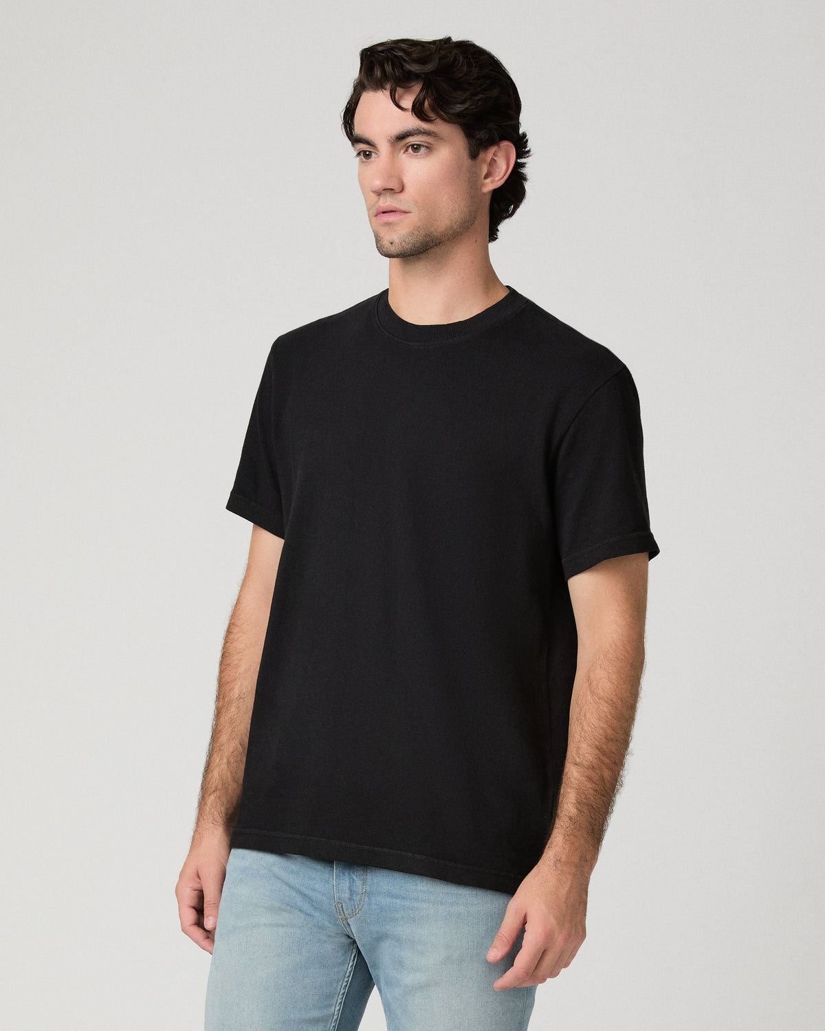 Man wearing black tee and light wash jeans against a black background