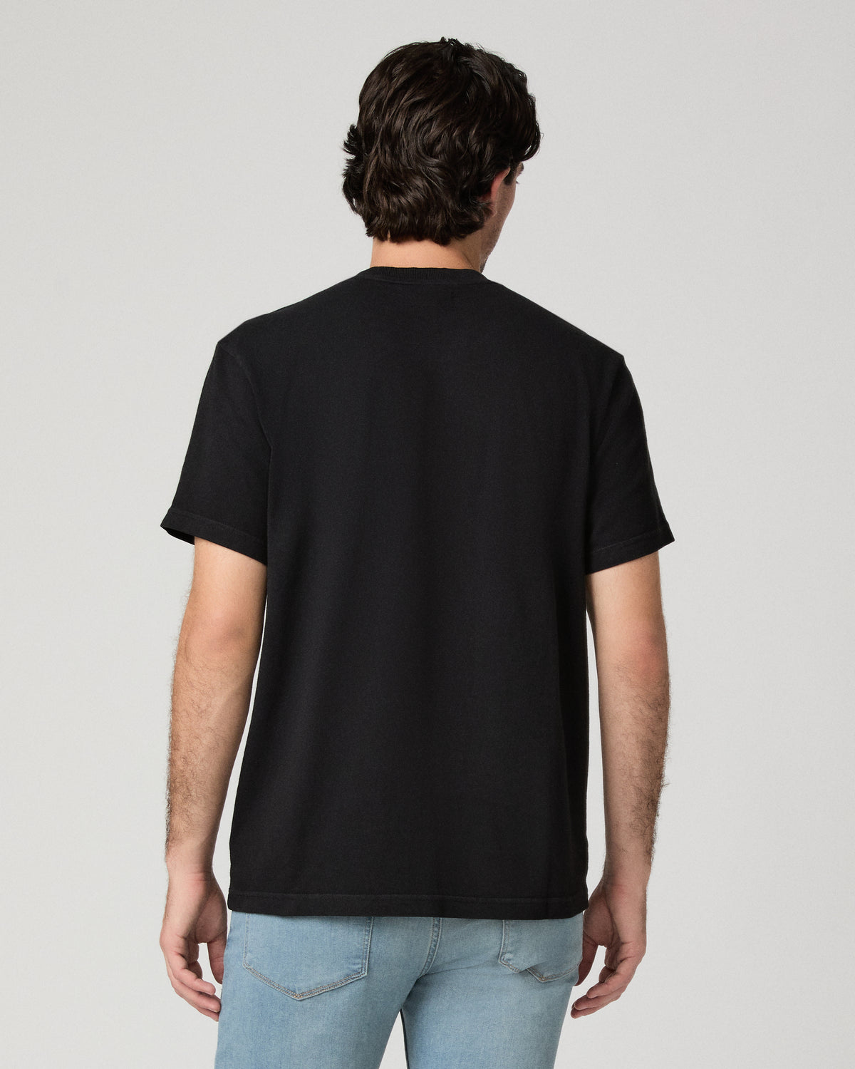 Man wearing black tee and light wash jeans against a black background