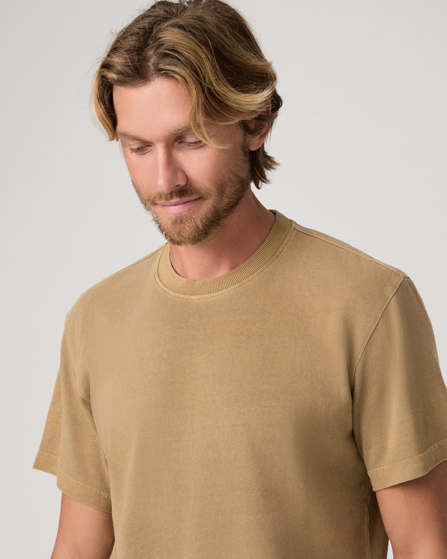 A man modeling a brown tee and dark green trousers against a light gray studio background.