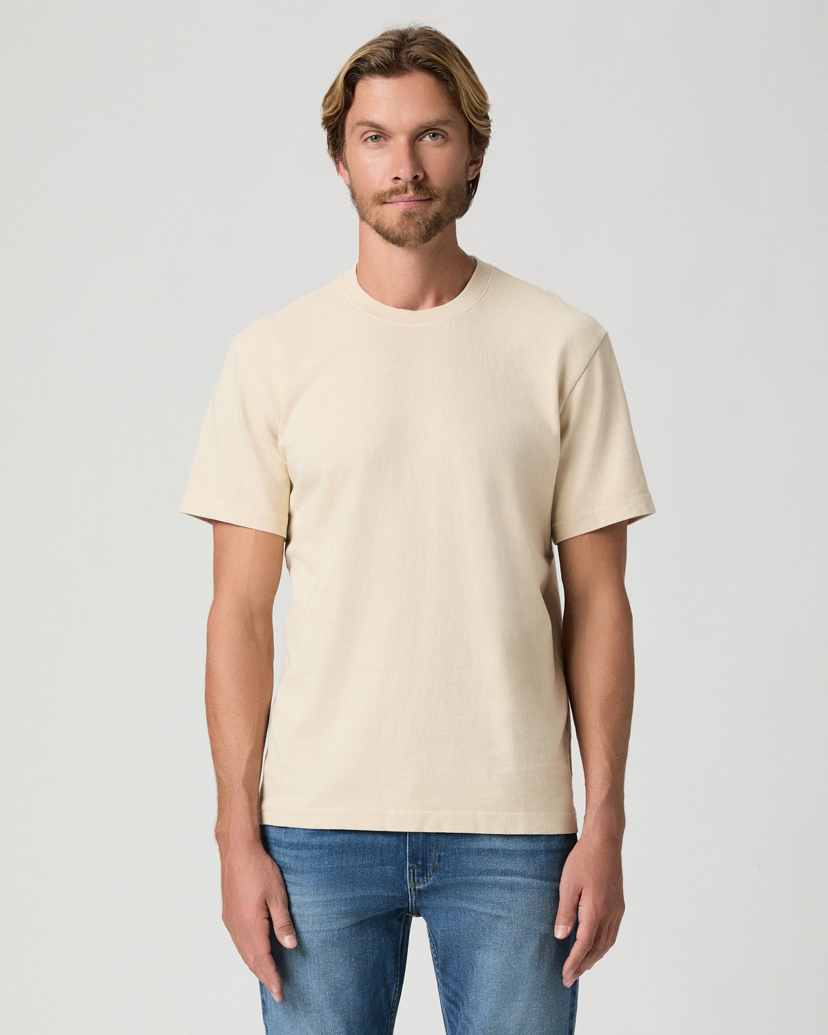 Model standing with arms at his sides, wearing the Serano Boxy Tee in Pale Antler, a cream short-sleeve tee, with medium-wash jeans