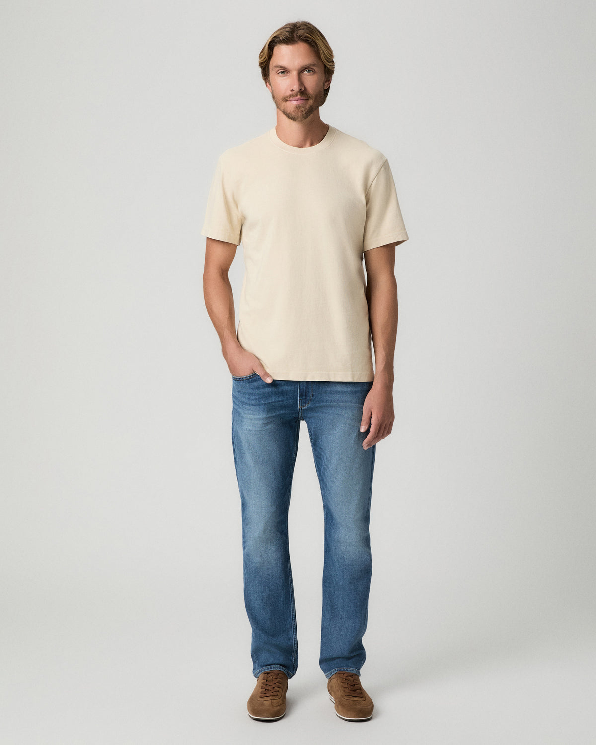 Full-length view of model with one hand in his pocket, wearing the Serano Boxy Tee in Pale Antler with medium-wash jeans and brown suede shoes
