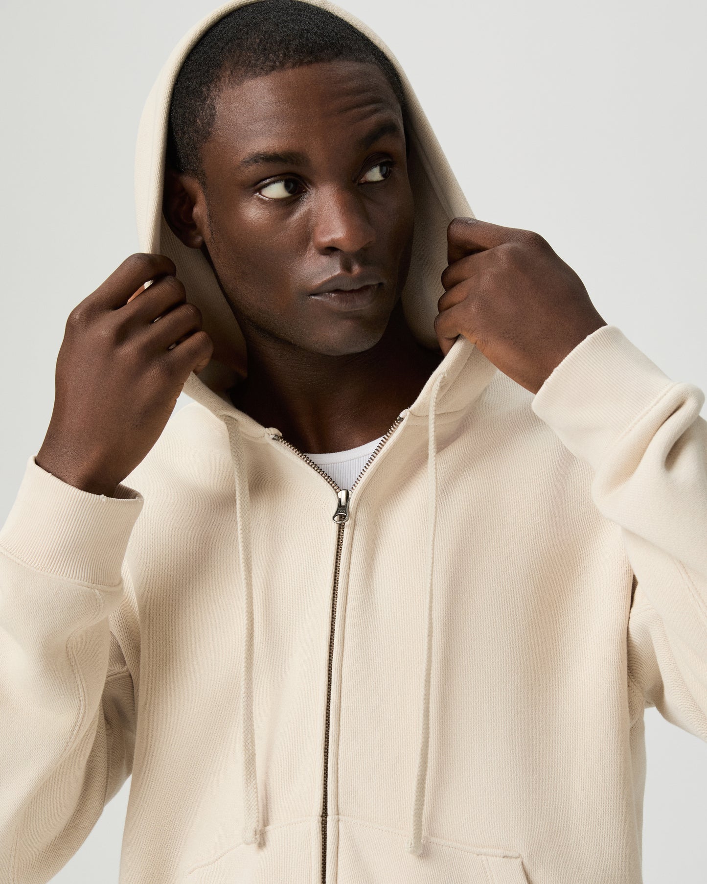 Man wearing a beige hoodie and light blue jeans on a white background