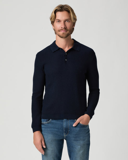 Model standing with one hand in his pocket, wearing the Selwyn Sweater Polo in Deep Anchor, a navy long-sleeve knit polo, with medium-wash jeans
