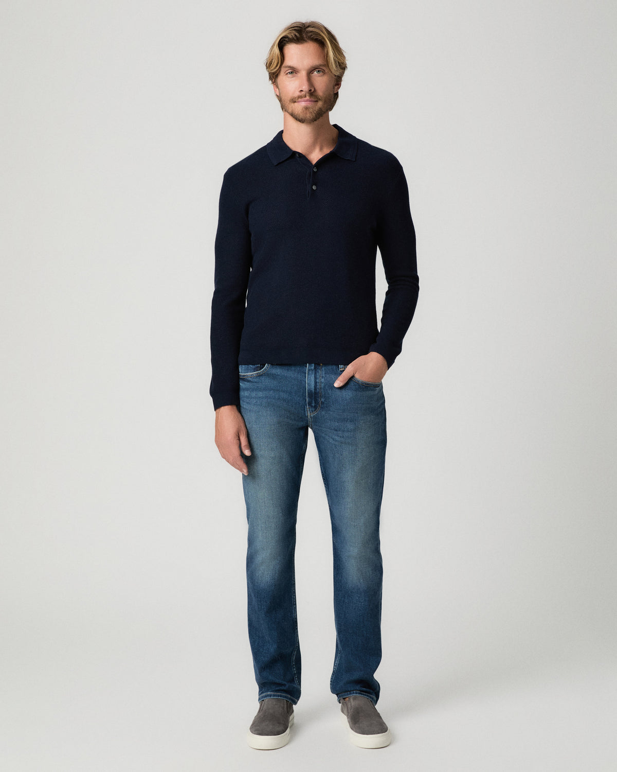Full-length view of model with one hand in his pocket, wearing the Selwyn Sweater Polo in Deep Anchor with medium-wash jeans and grey suede shoes