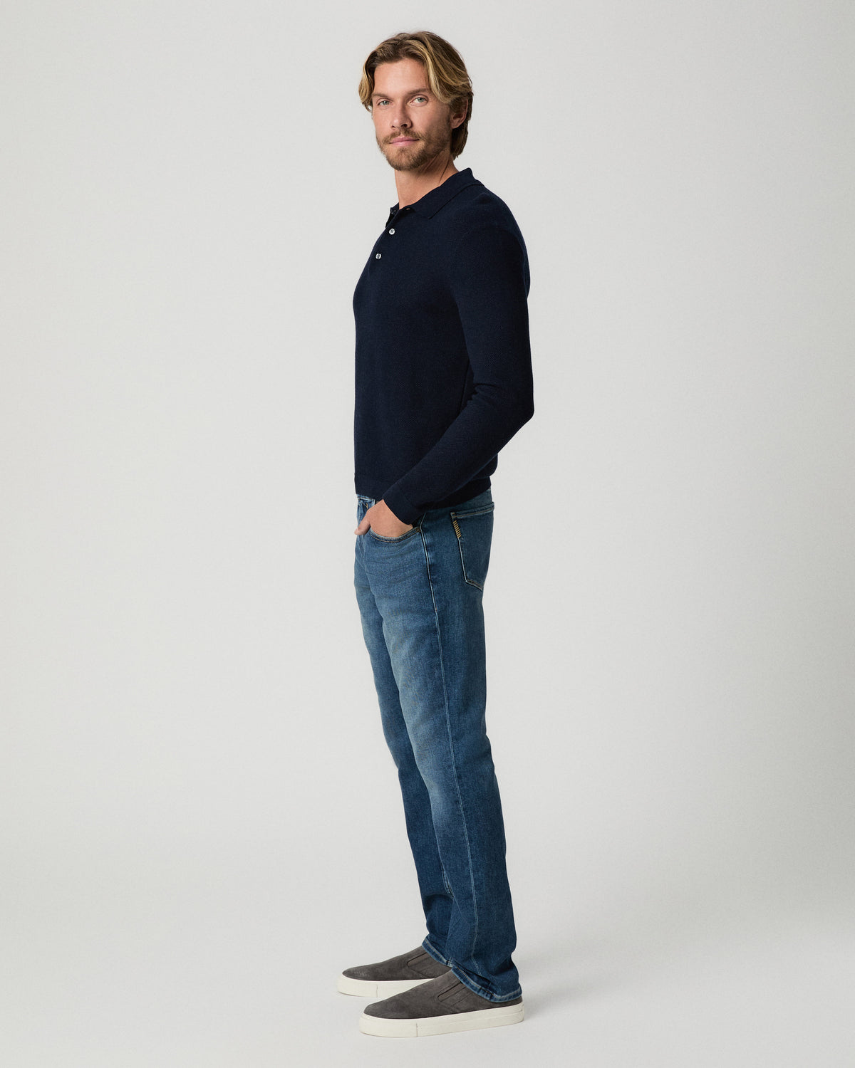 Side profile of model with one hand in his pocket, wearing the Selwyn Sweater Polo in Deep Anchor with medium-wash jeans and grey suede shoes