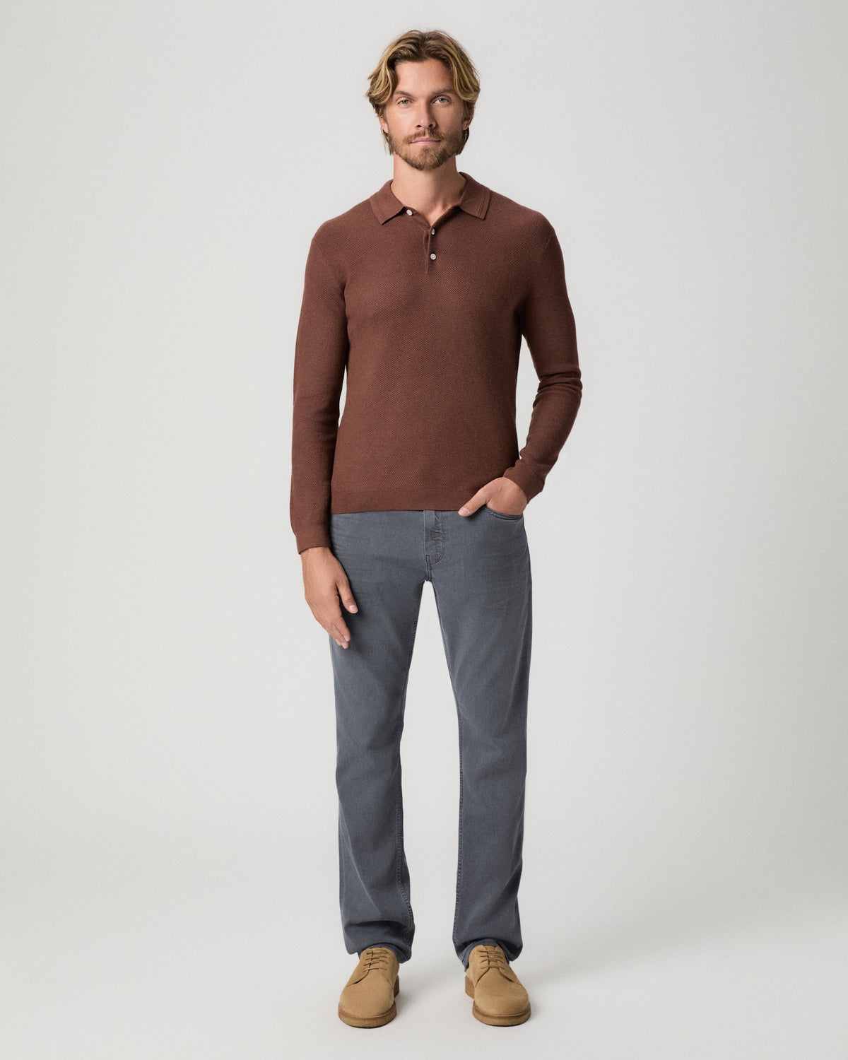 Full-length view of model with one hand in his pocket, wearing the Selwyn Sweater Polo in Sorrel with grey jeans and tan suede boots