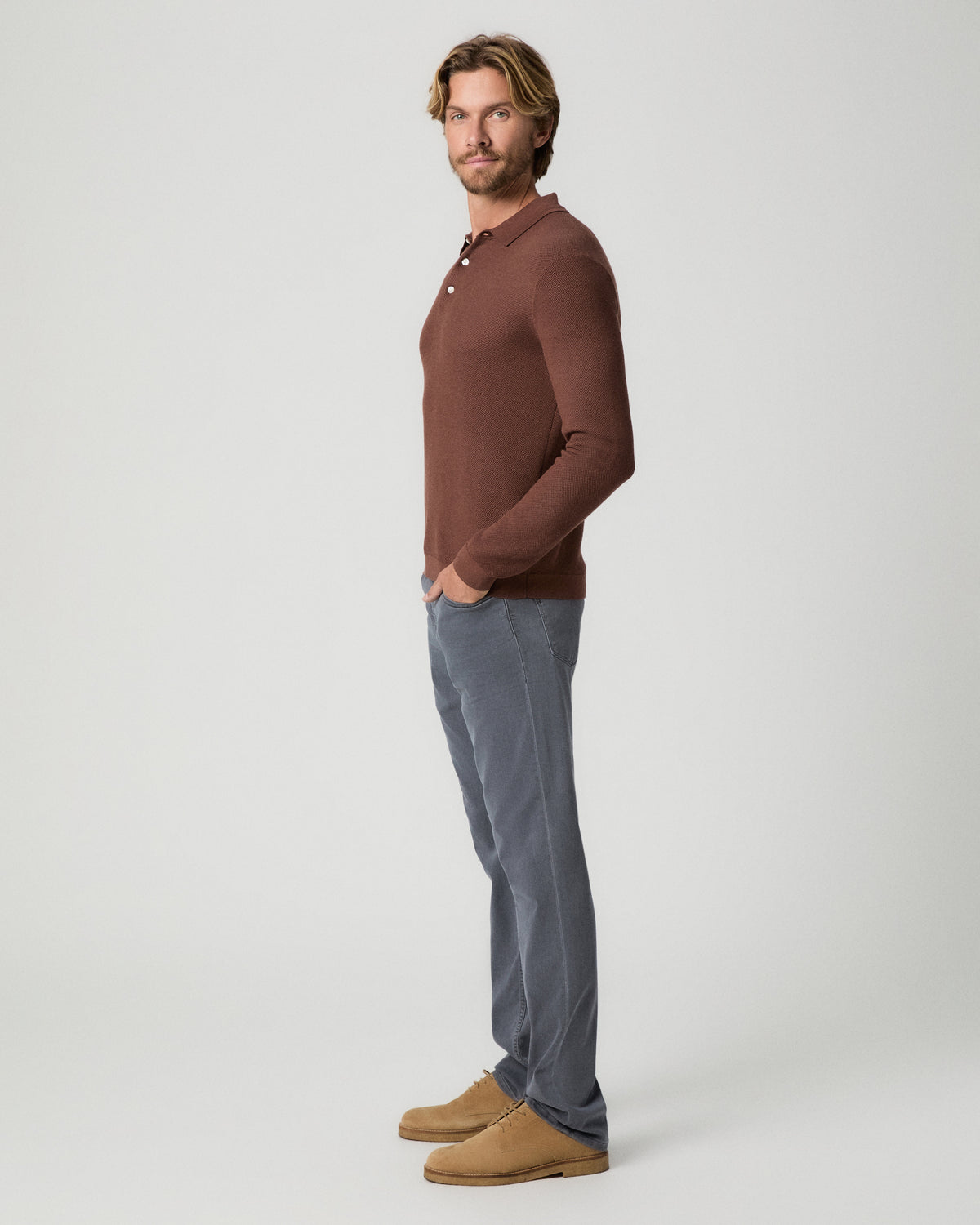 Side profile of model with one hand in his pocket, wearing the Selwyn Sweater Polo in Sorrel with grey jeans and tan suede boots