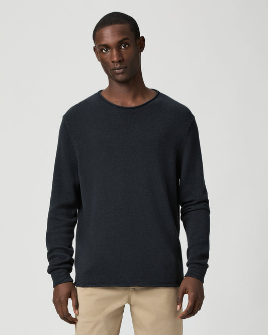 Man wearing a dark blue sweater and beige pants on a light gray background
