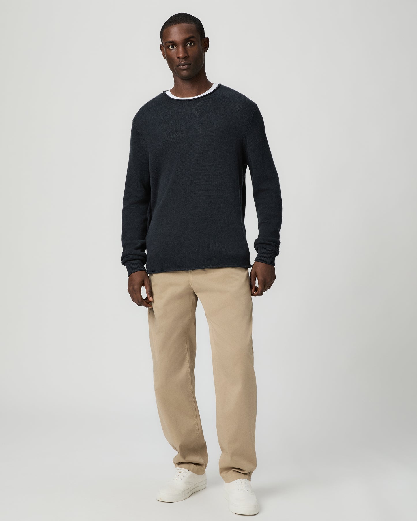 Man wearing a dark blue sweater and beige pants on a light gray background