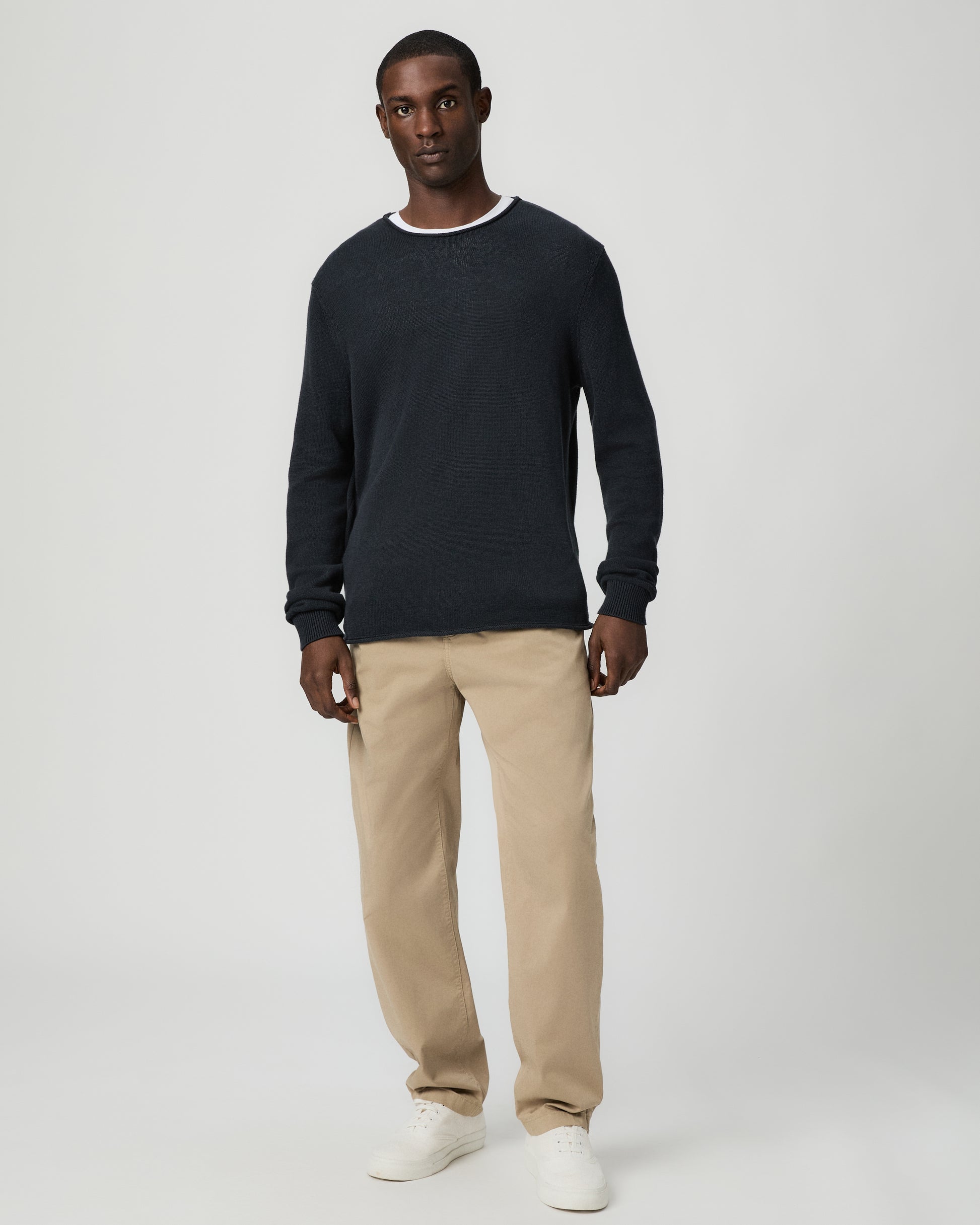 Man wearing a dark blue sweater and beige pants on a light gray background