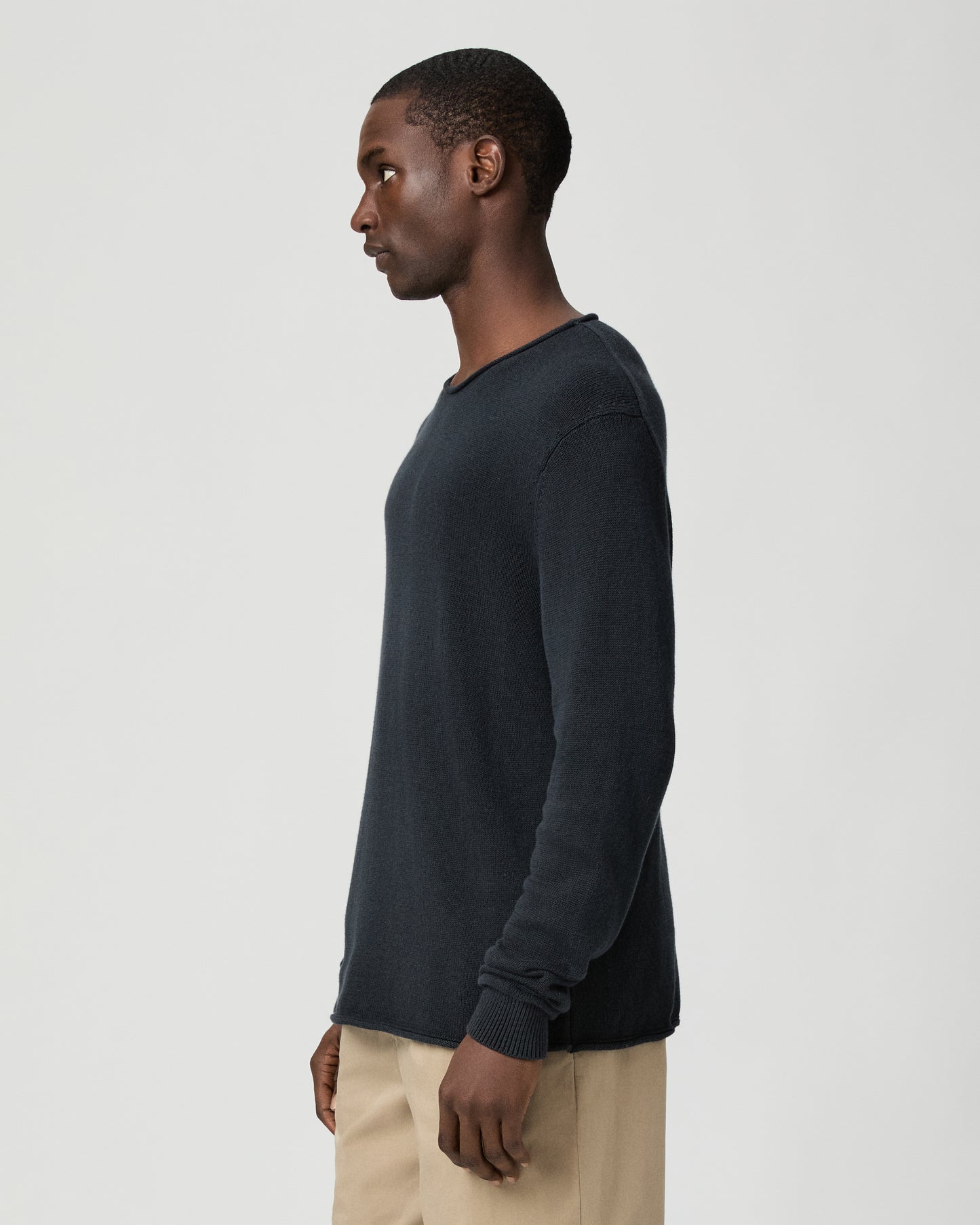 Man wearing a dark blue sweater and beige pants on a light gray background