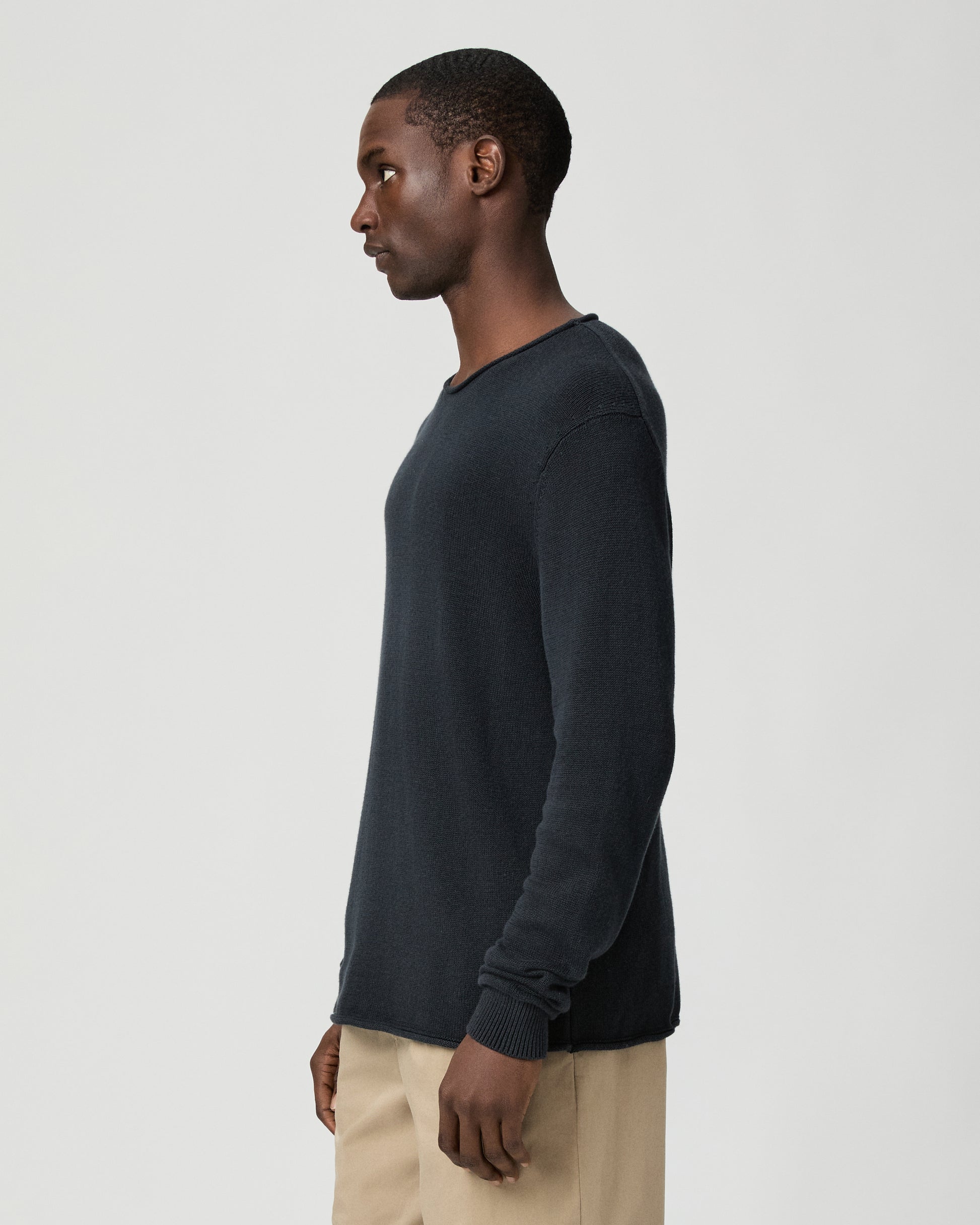 Man wearing a dark blue sweater and beige pants on a light gray background