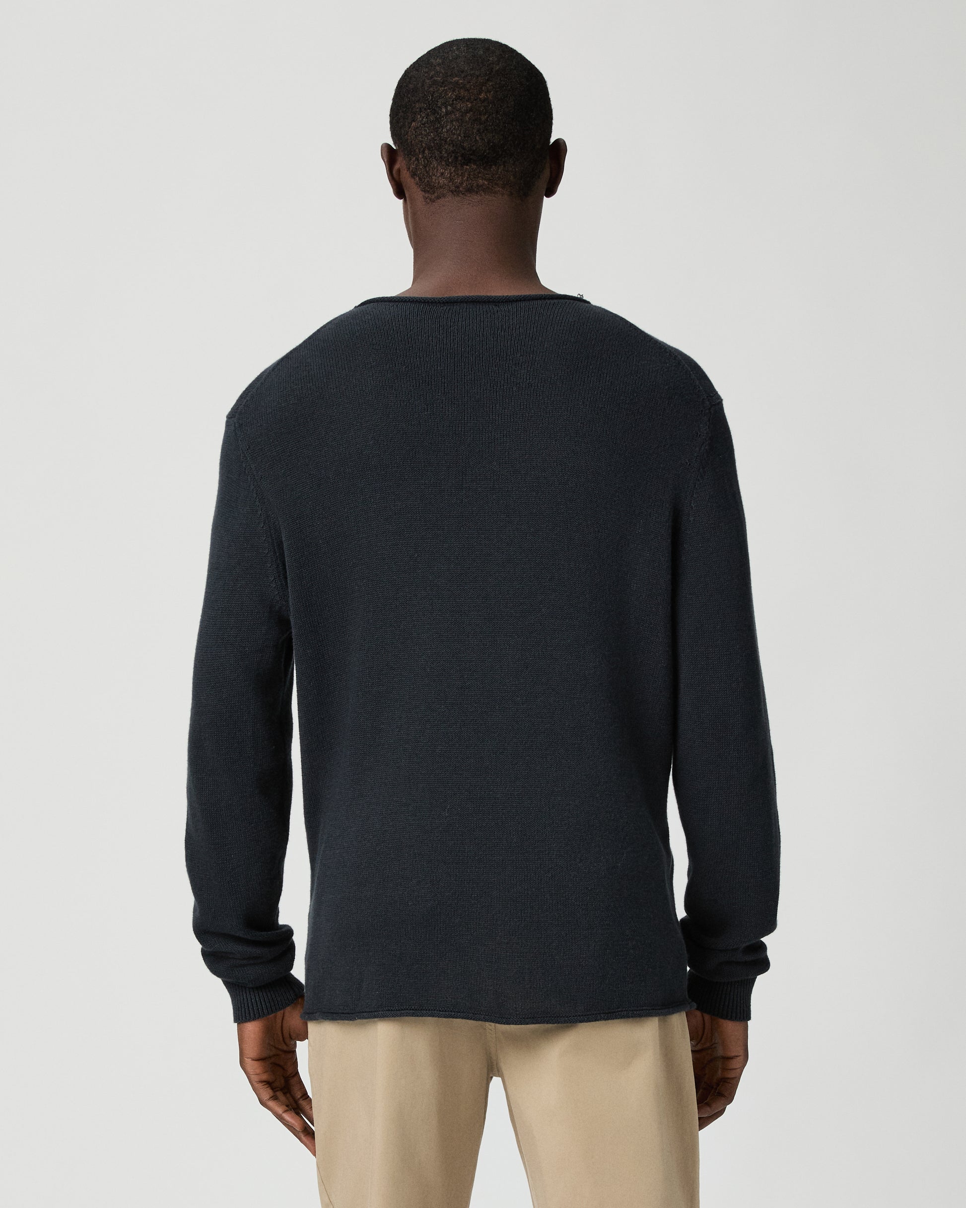 Man wearing a dark blue sweater and beige pants on a light gray background