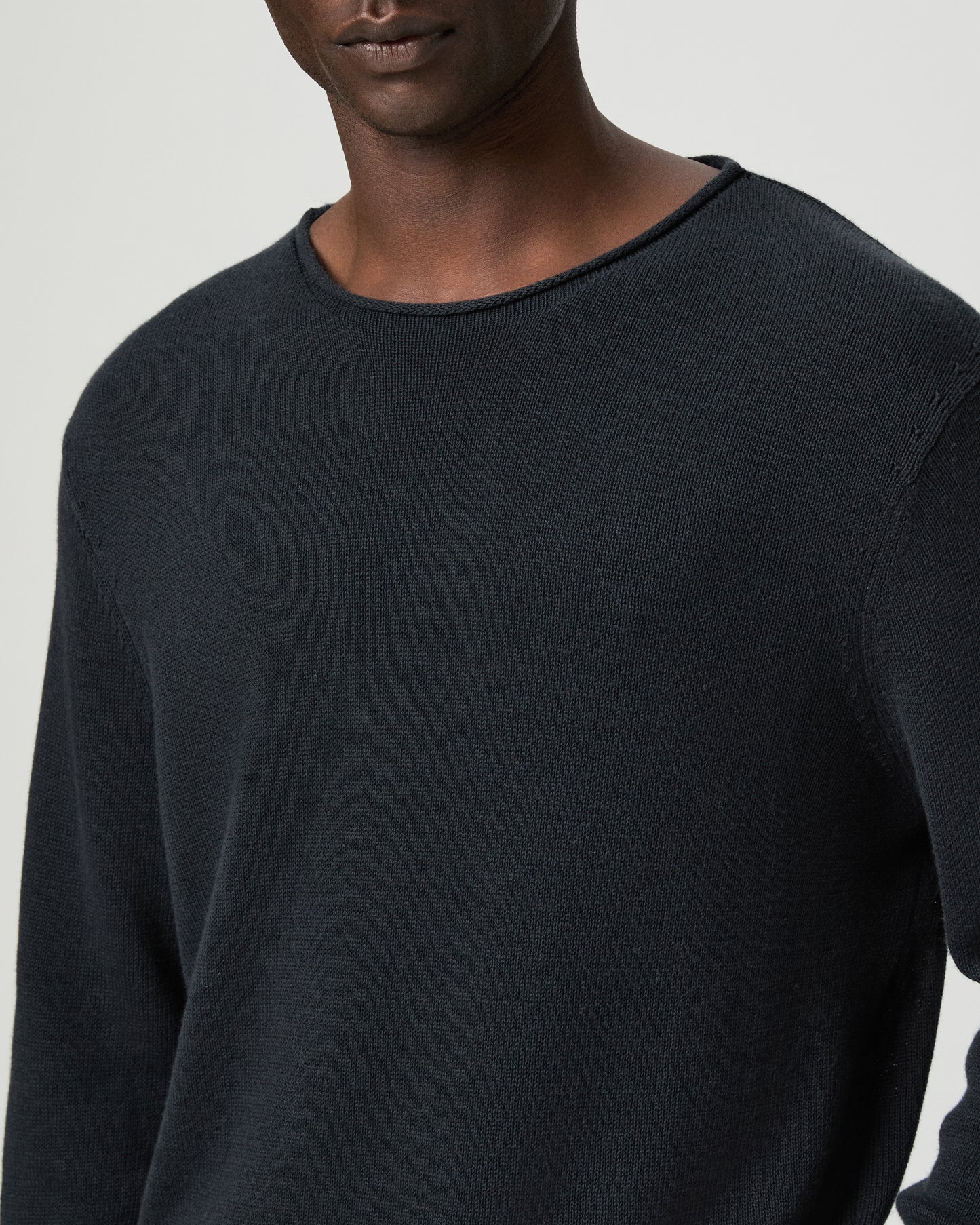 Man wearing a dark blue sweater and beige pants on a light gray background