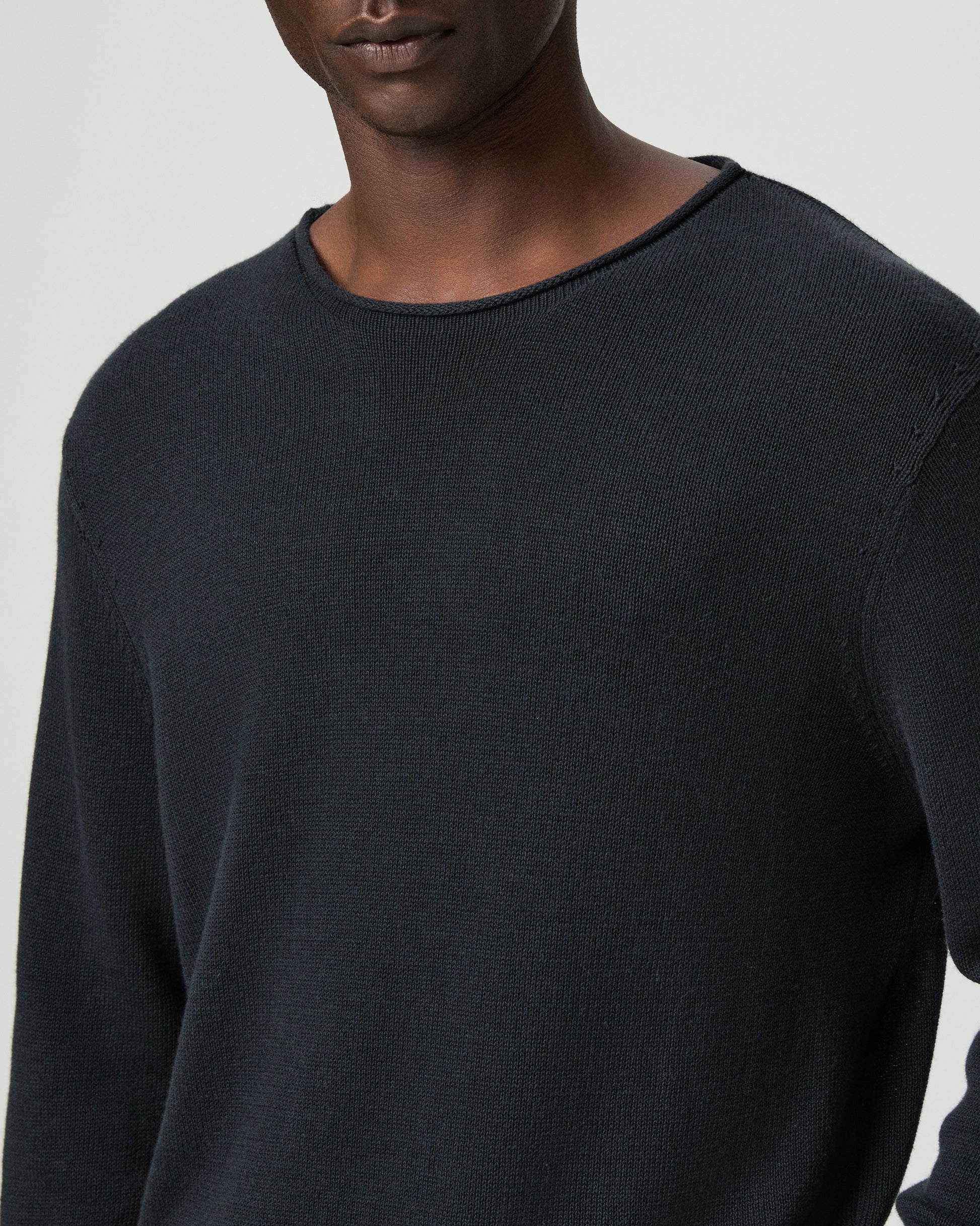 Man wearing a dark blue sweater and beige pants on a light gray background