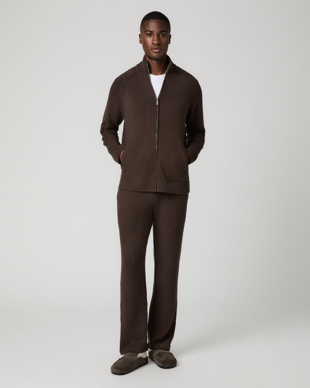 Full-length front view of a man wearing the chocolate brown zip-up cardigan over a white t-shirt with matching brown sweatpants and brown slides, one hand in his pocket.