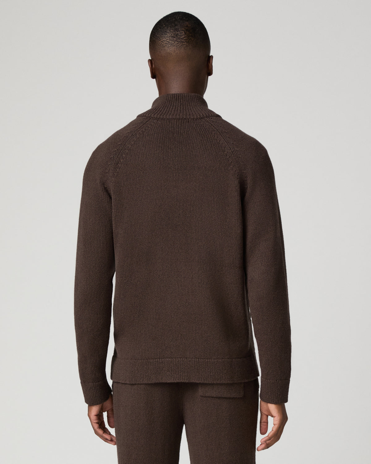 Back view of a man wearing the chocolate brown zip-up cardigan, showing the ribbed knit texture and raglan sleeve seams, paired with matching brown pants.