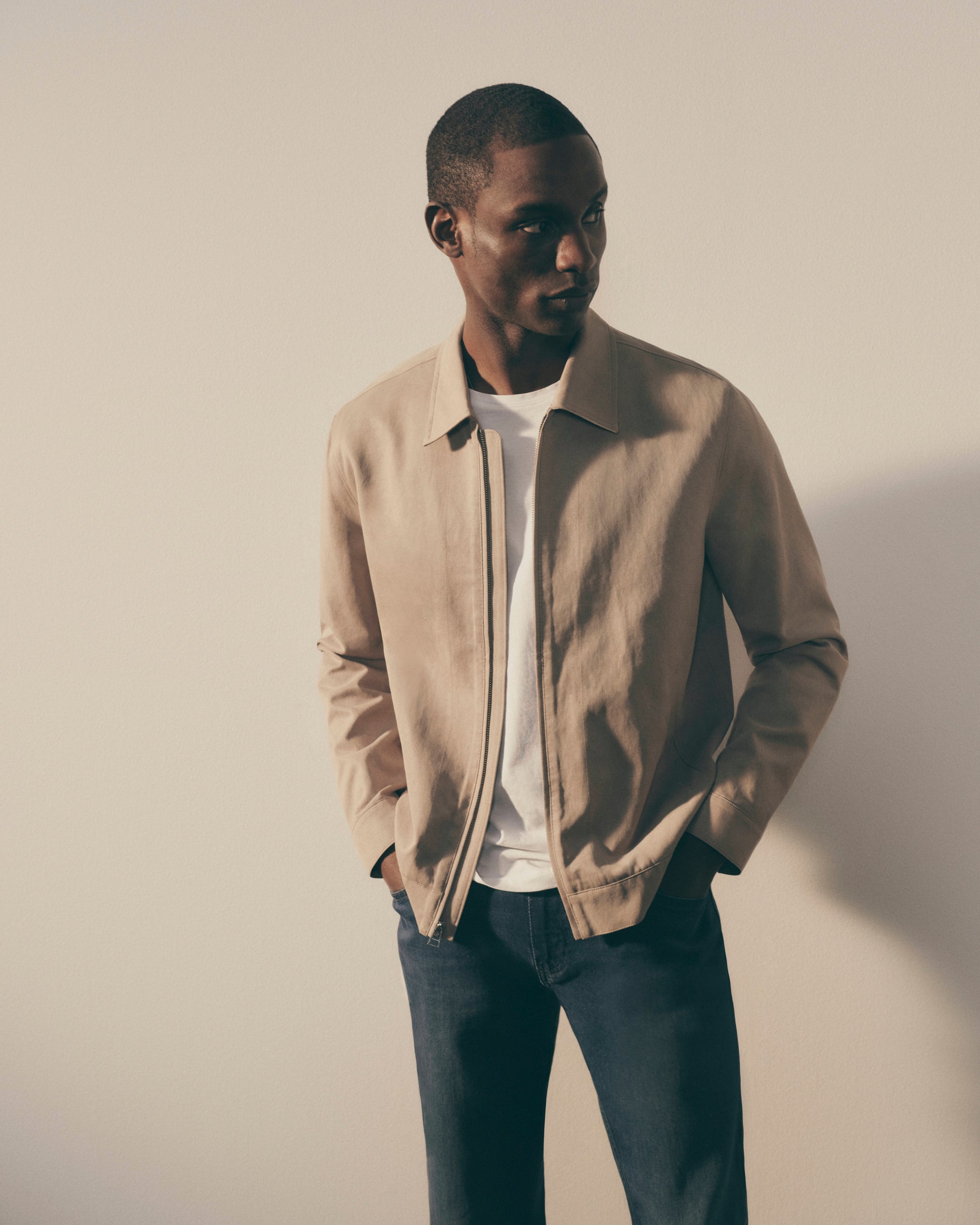 Man wearing a beige jacket over a white shirt with a neutral background
