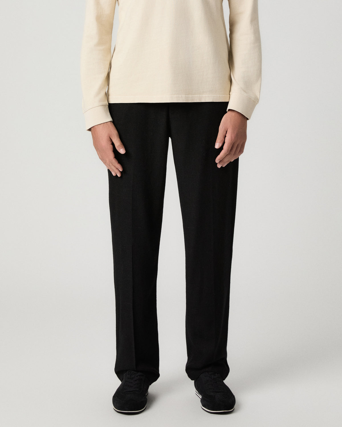 Front view from the waist down of the Tiano Pant in Black, a straight-leg pant, worn with a cream sweater and black shoes