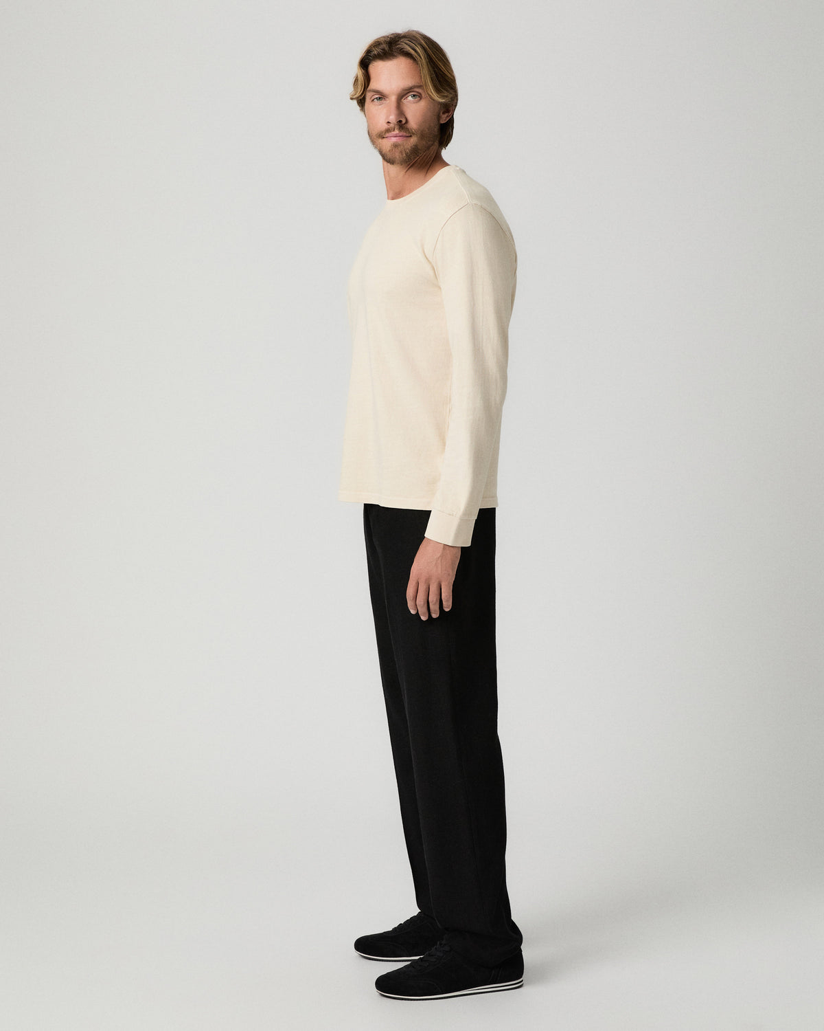 Side profile of model wearing a cream sweater with the Tiano Pant in Black and black shoes