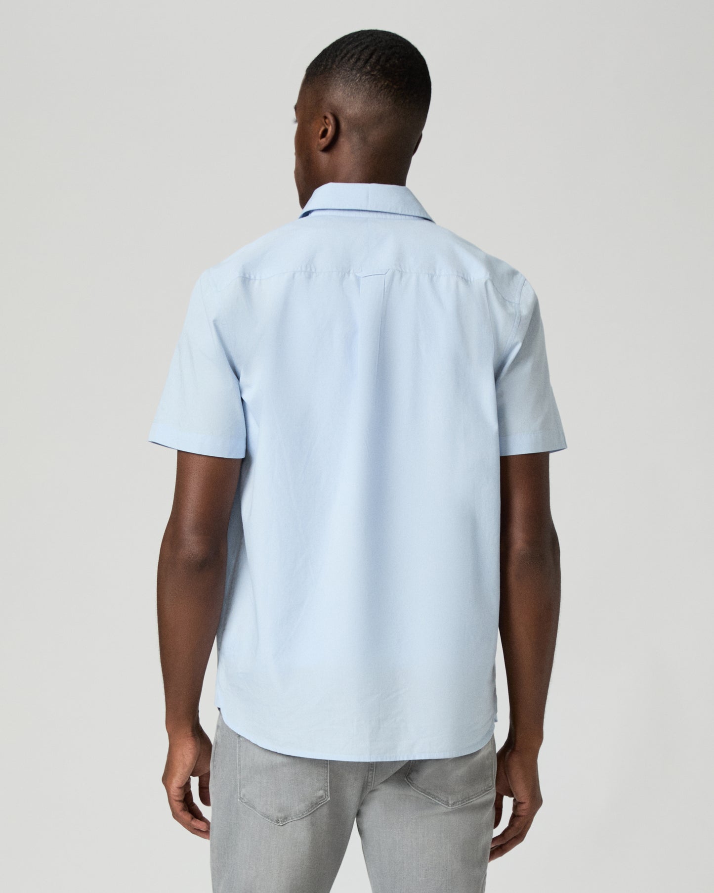 Man wearing a light blue short-sleeve shirt over a white t-shirt on a plain background