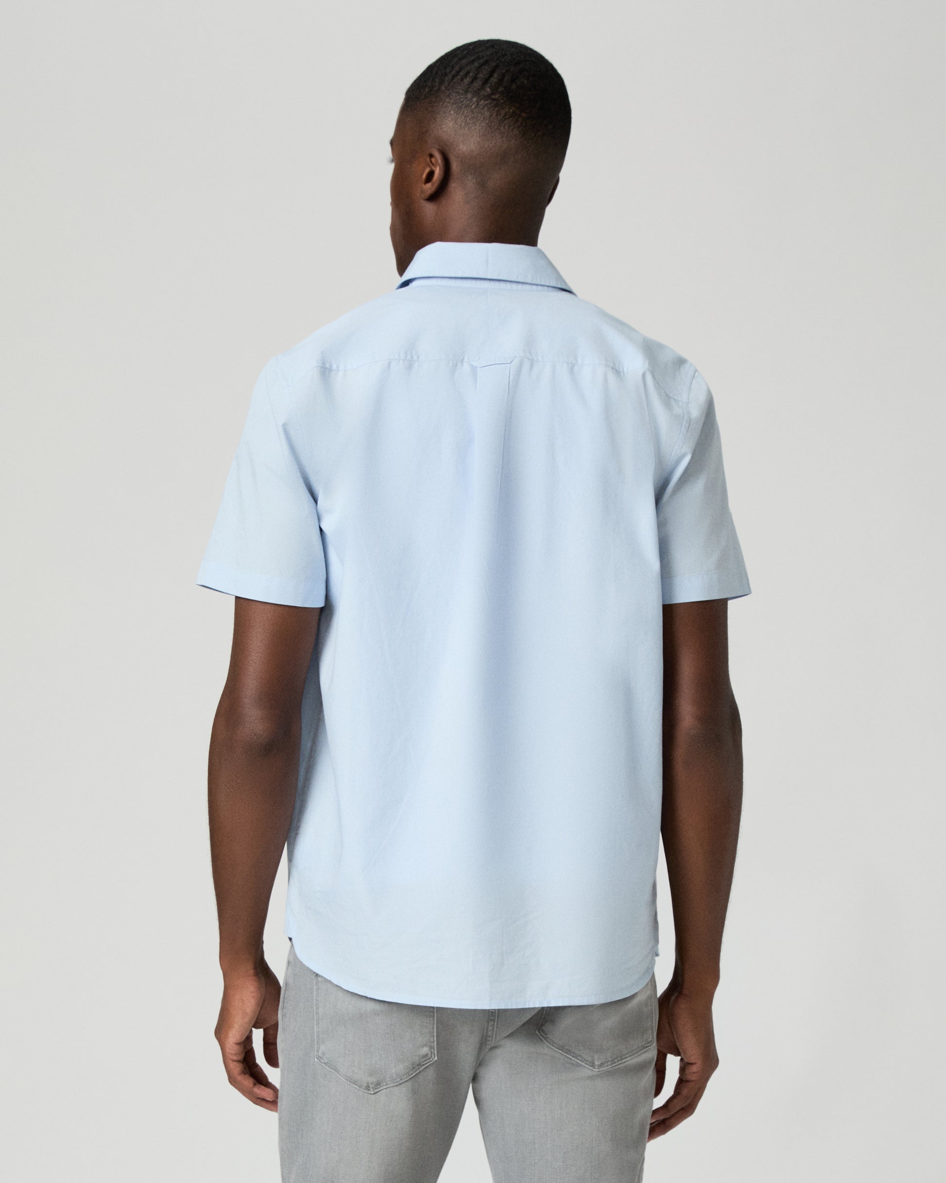 Man wearing a light blue short-sleeve shirt over a white t-shirt on a plain background