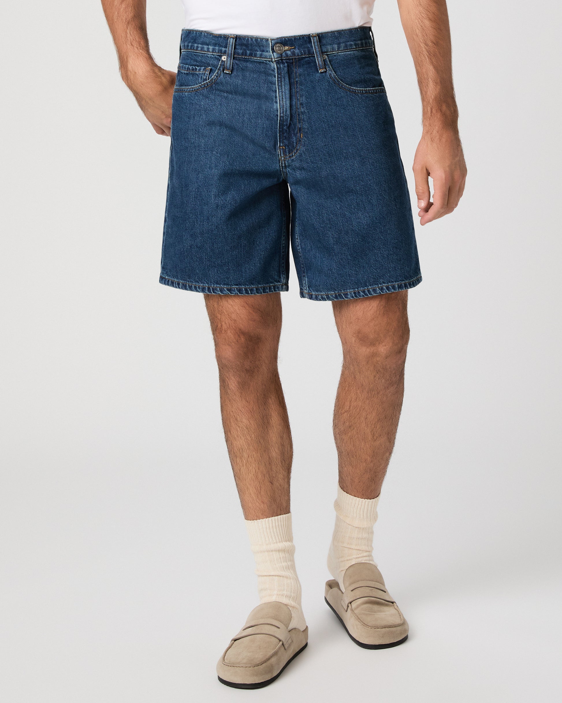 Man wearing a white t-shirt, blue shorts, and beige shoes on a white background