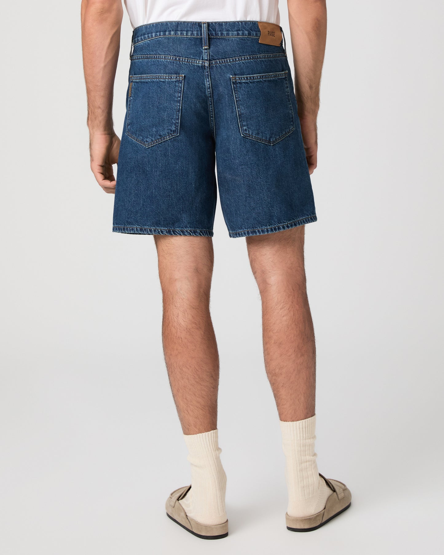 Man wearing a white t-shirt, blue shorts, and beige shoes on a white background