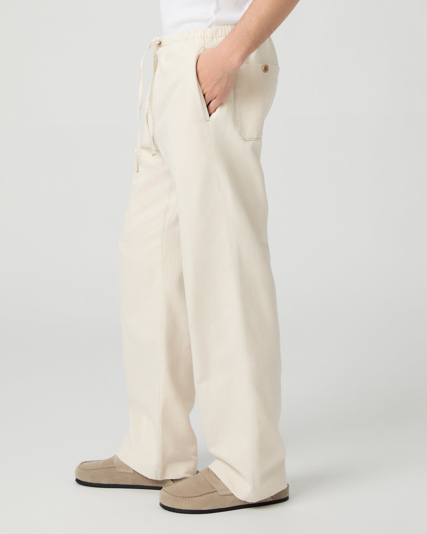 Man wearing a white tee and beige linen pants paired with grey shoes on a white background